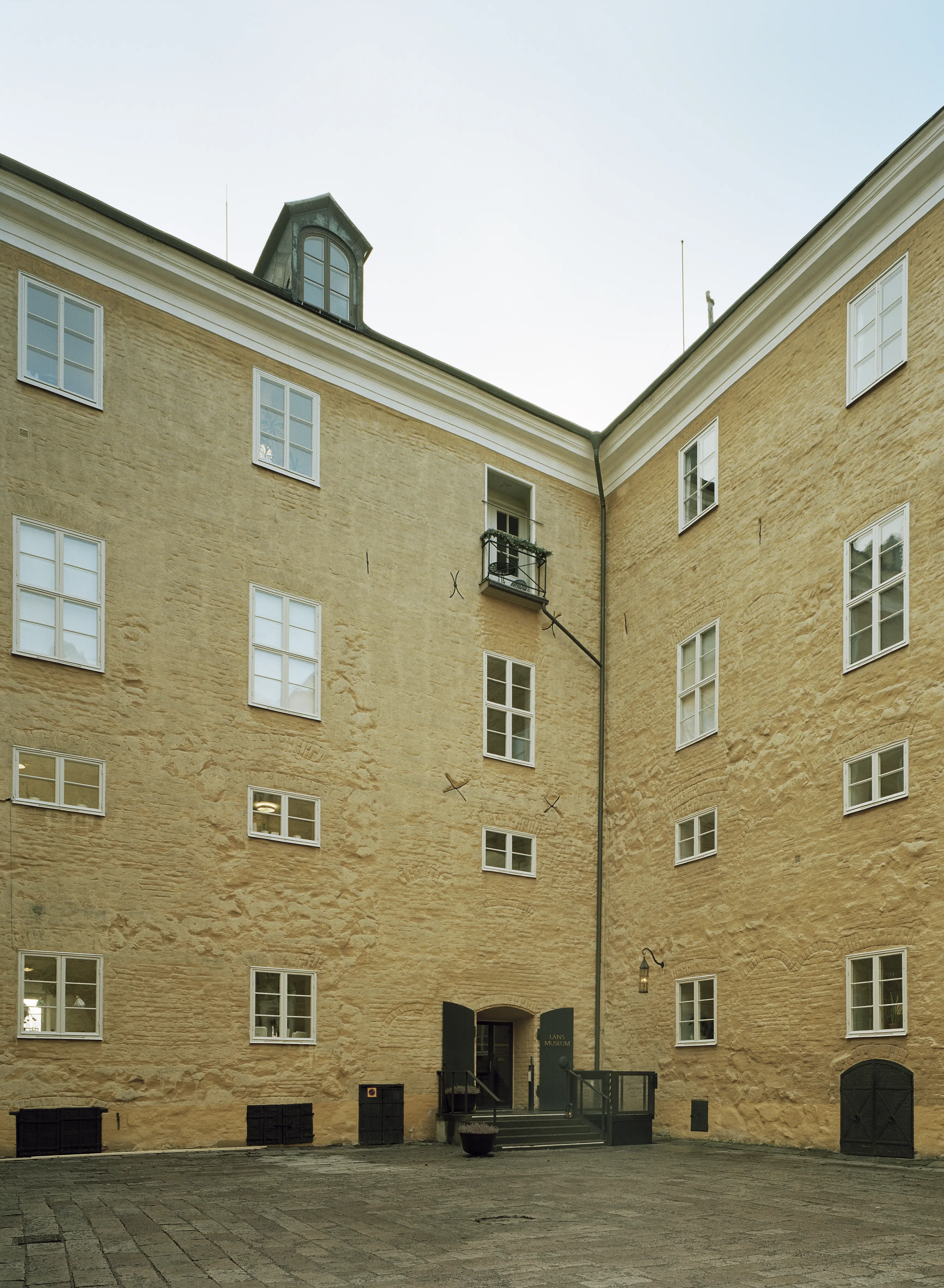 Västerås slott. Den stenlagda innergården. Fasaden mot gården är av tegel klädd i gul puts. En port leder in till länsmuseet.