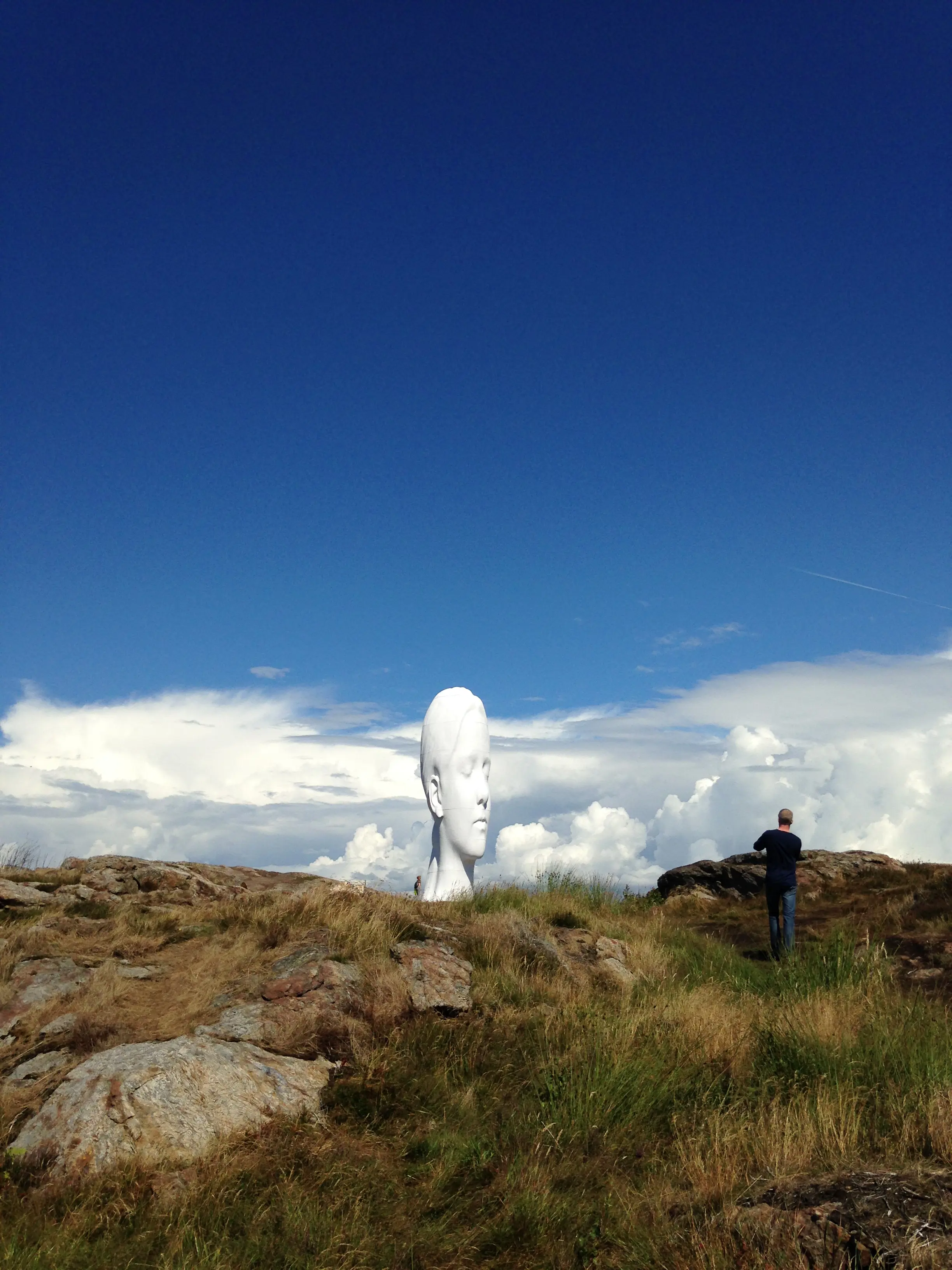 Gigantiskt vitt kvinnohuvud på berg med dramatisk molnhimmel.