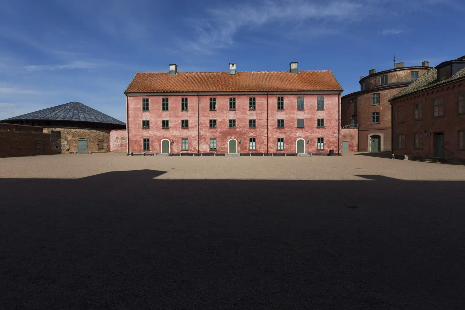 Ett hus i tre våningar med rosa fasad och rött taktegel, omgivet av runda torn.