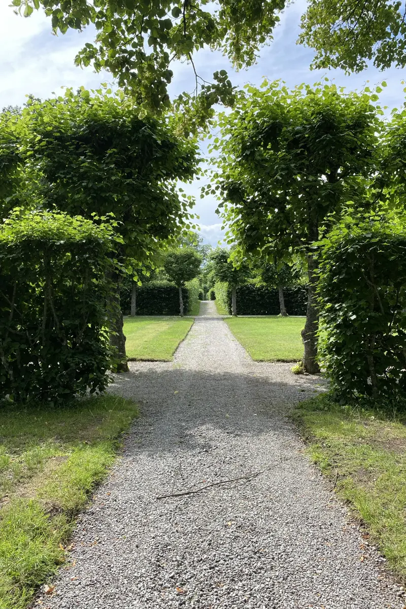 Drottningholms slottspark, vid Kina slott. En grusväg går mellan omväxlande häckar, gräsytor och formklippta träd.