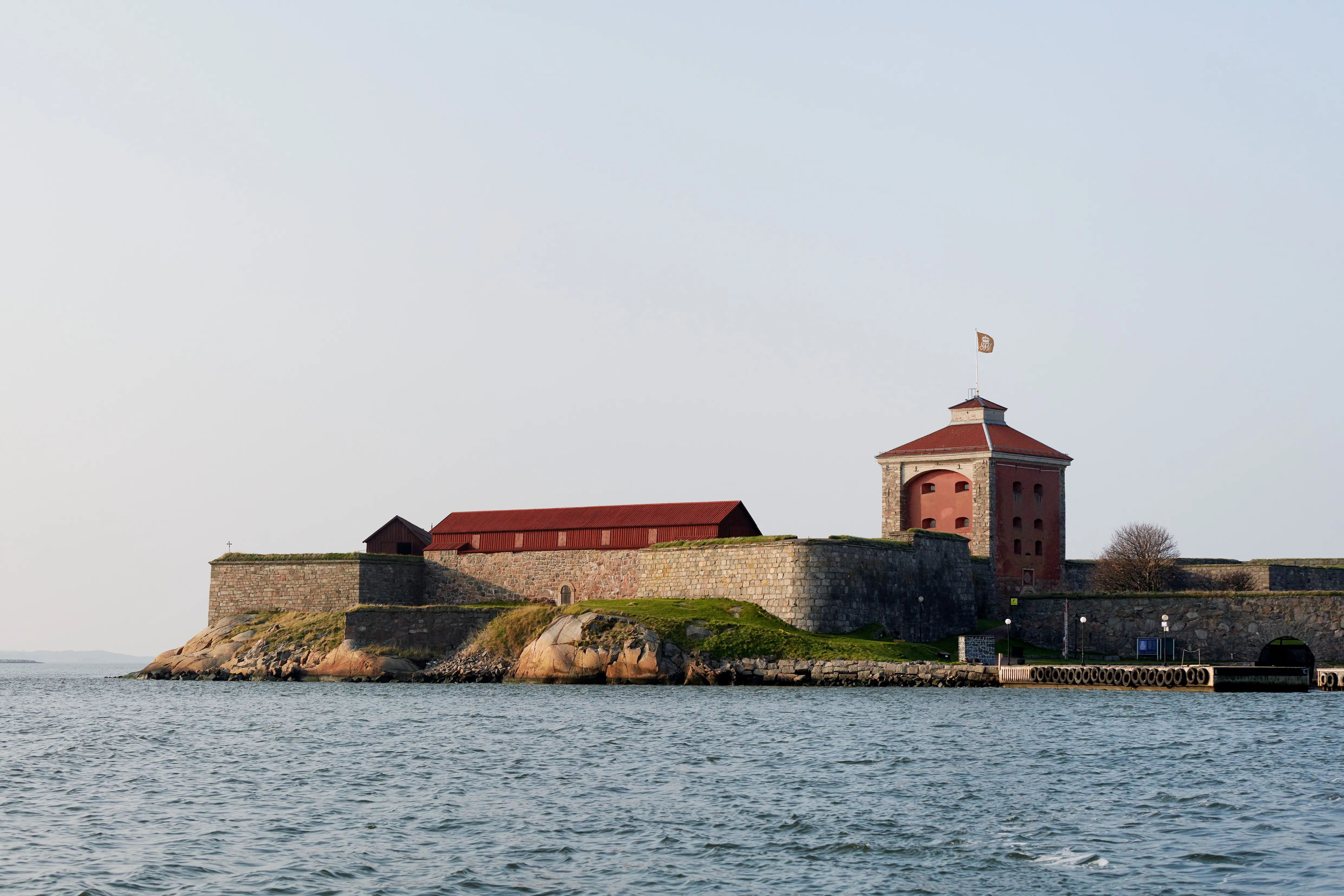 Nya Älvsborgs fästning sedd över vattnet. Det fyrkantiga tornet och kurtinernas röda fredstak höjer sig över bastionens stenmurar.