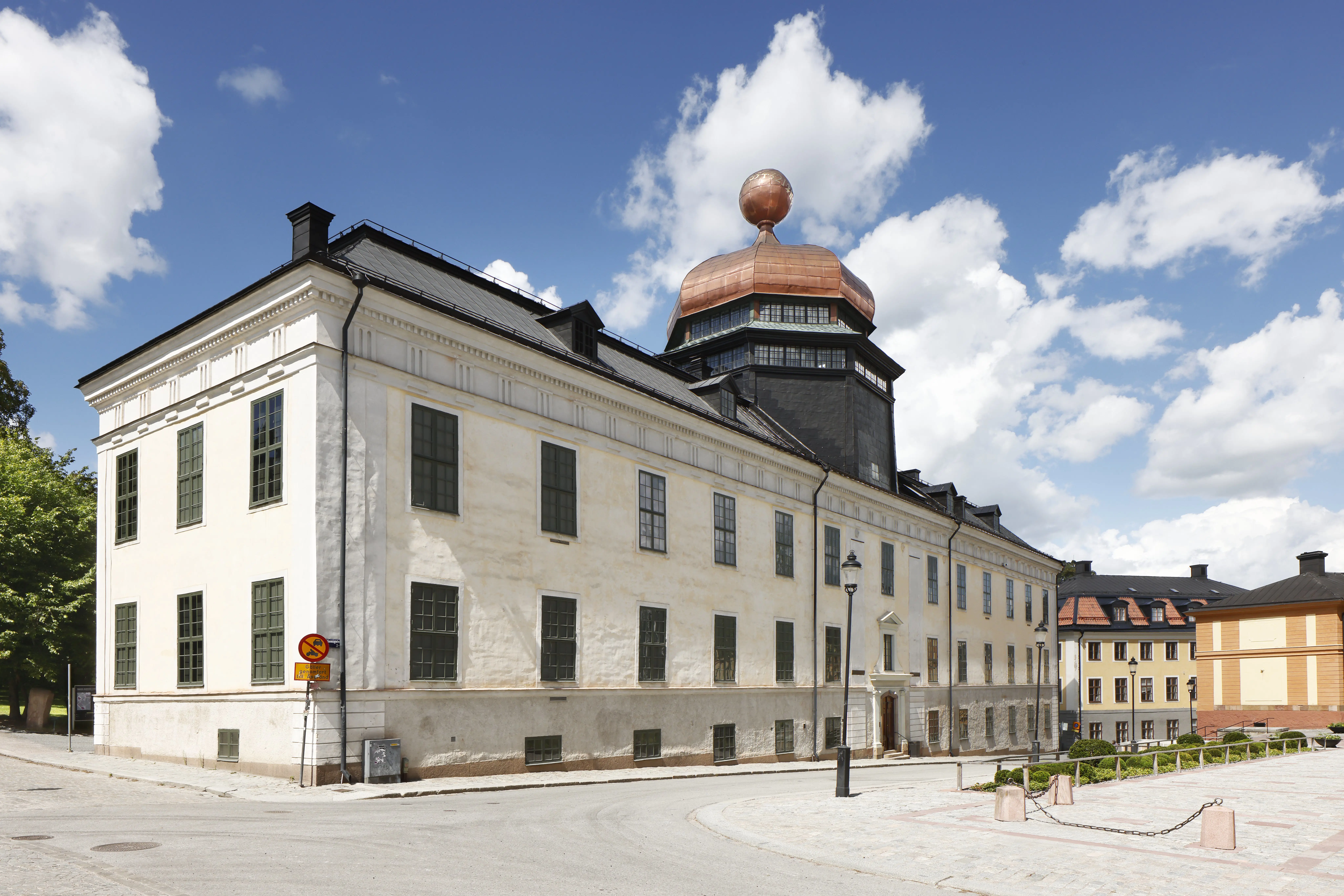 Gustavianum med närmiljö. Byggnaden har ny, gräddvit puts och tak-kupolens nya kopparplåt glänser röd.