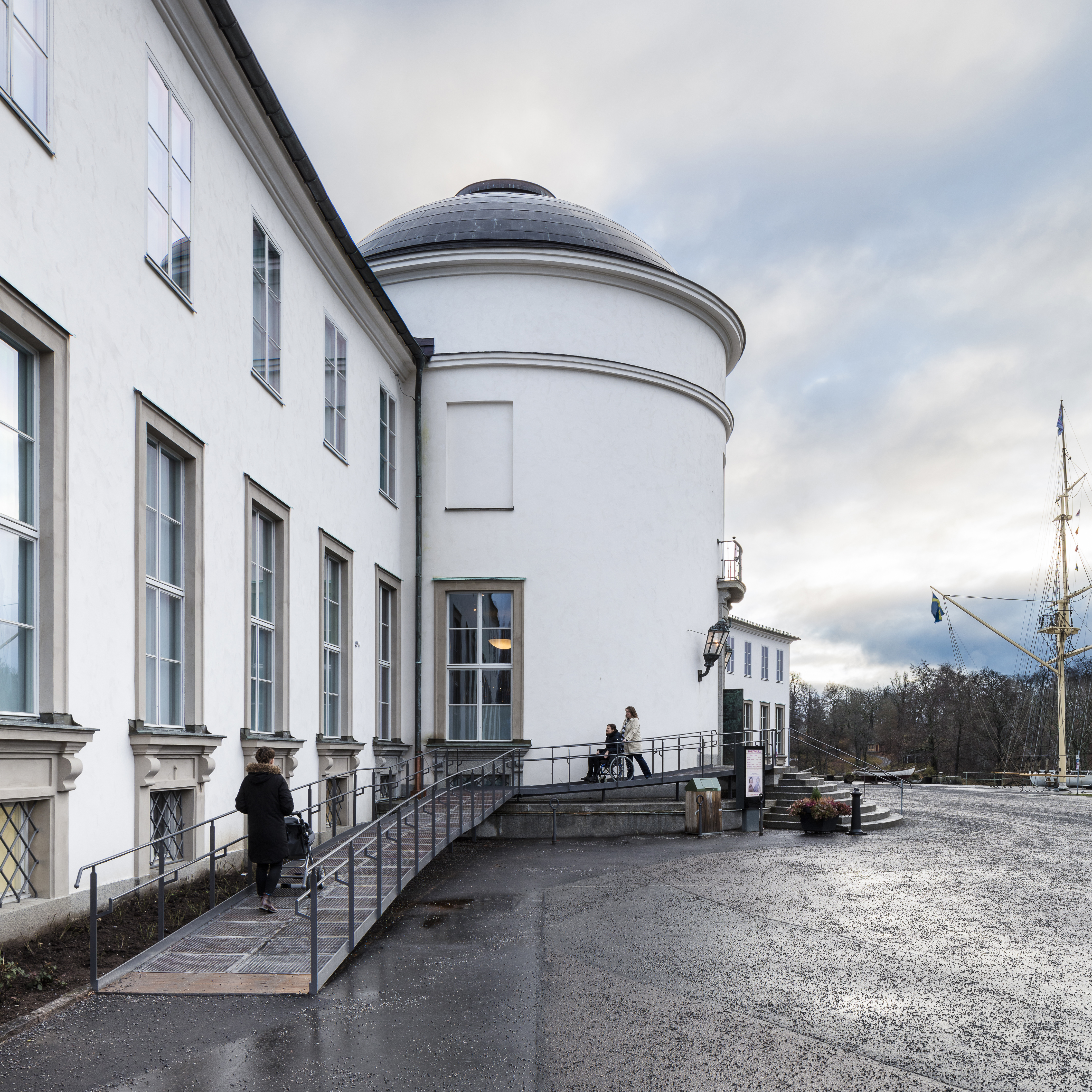 Sjöhistoriska museets tillgängliga entré. En person med barnvagn och två personer med en rullstol använder rampen.