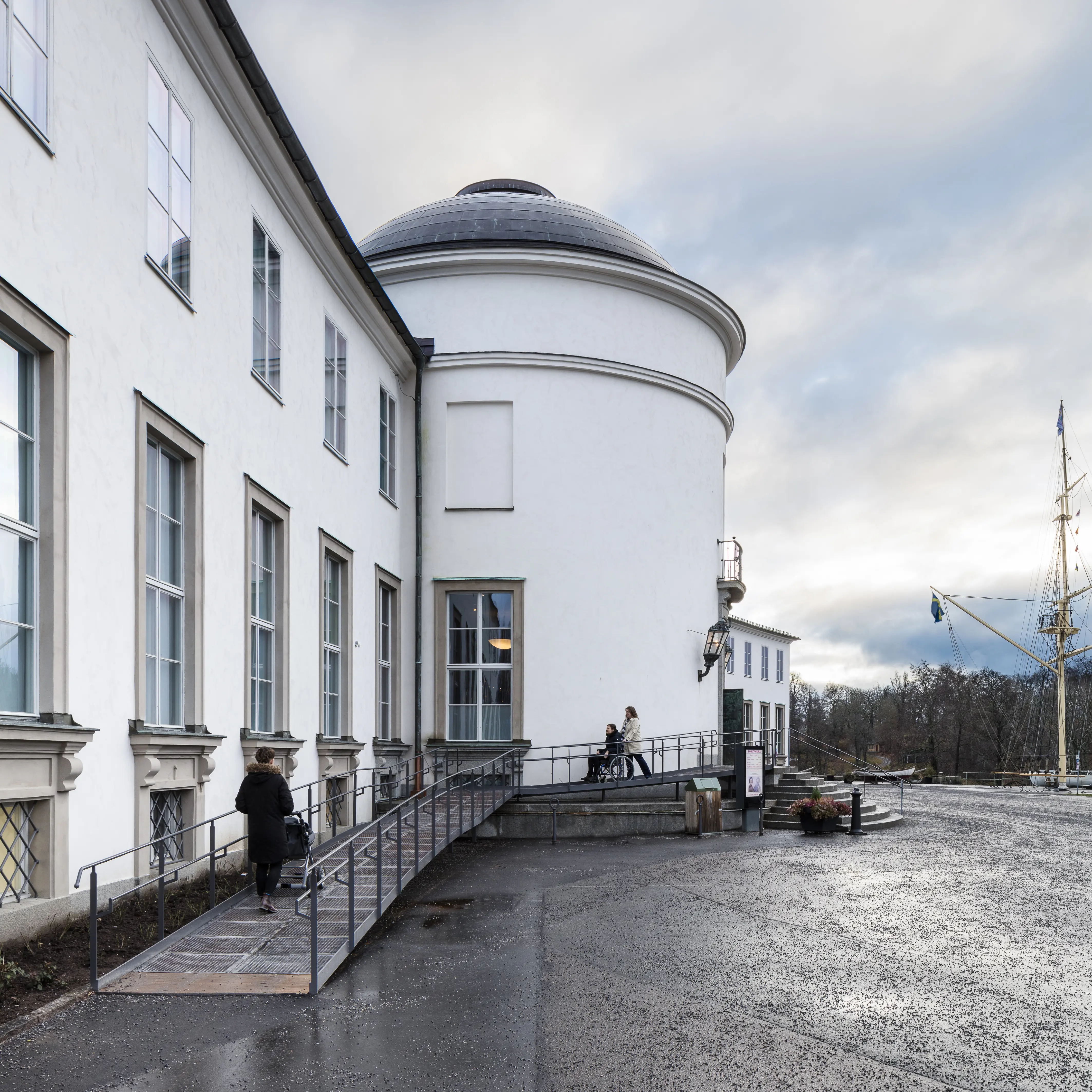 Sjöhistoriska museets tillgängliga entré. En person med barnvagn och två personer med en rullstol använder rampen.