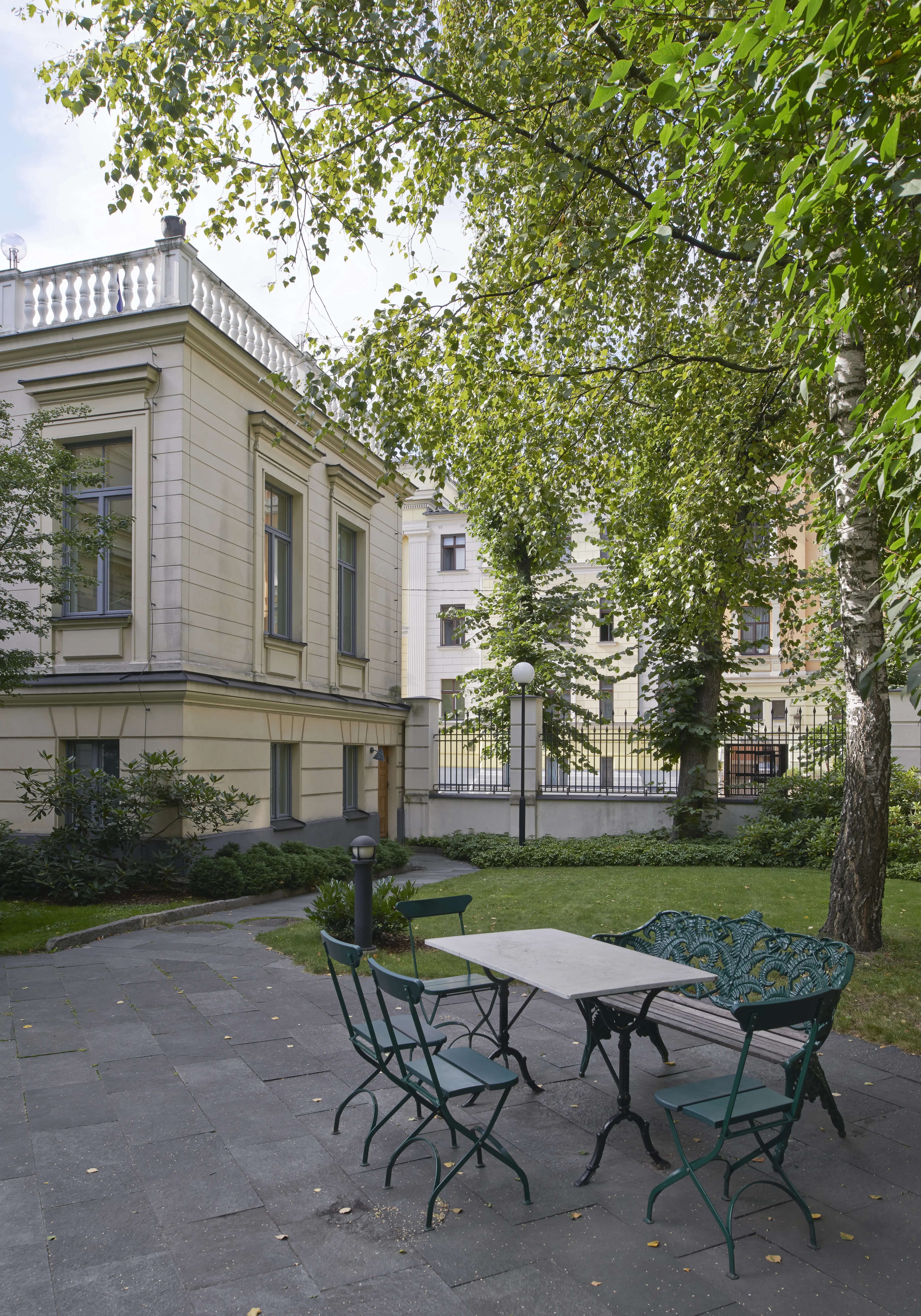 Trädgården vid ambassaden i Riga. På en stenlagd uteplats under ett par björkar står trädgårds-möbler.