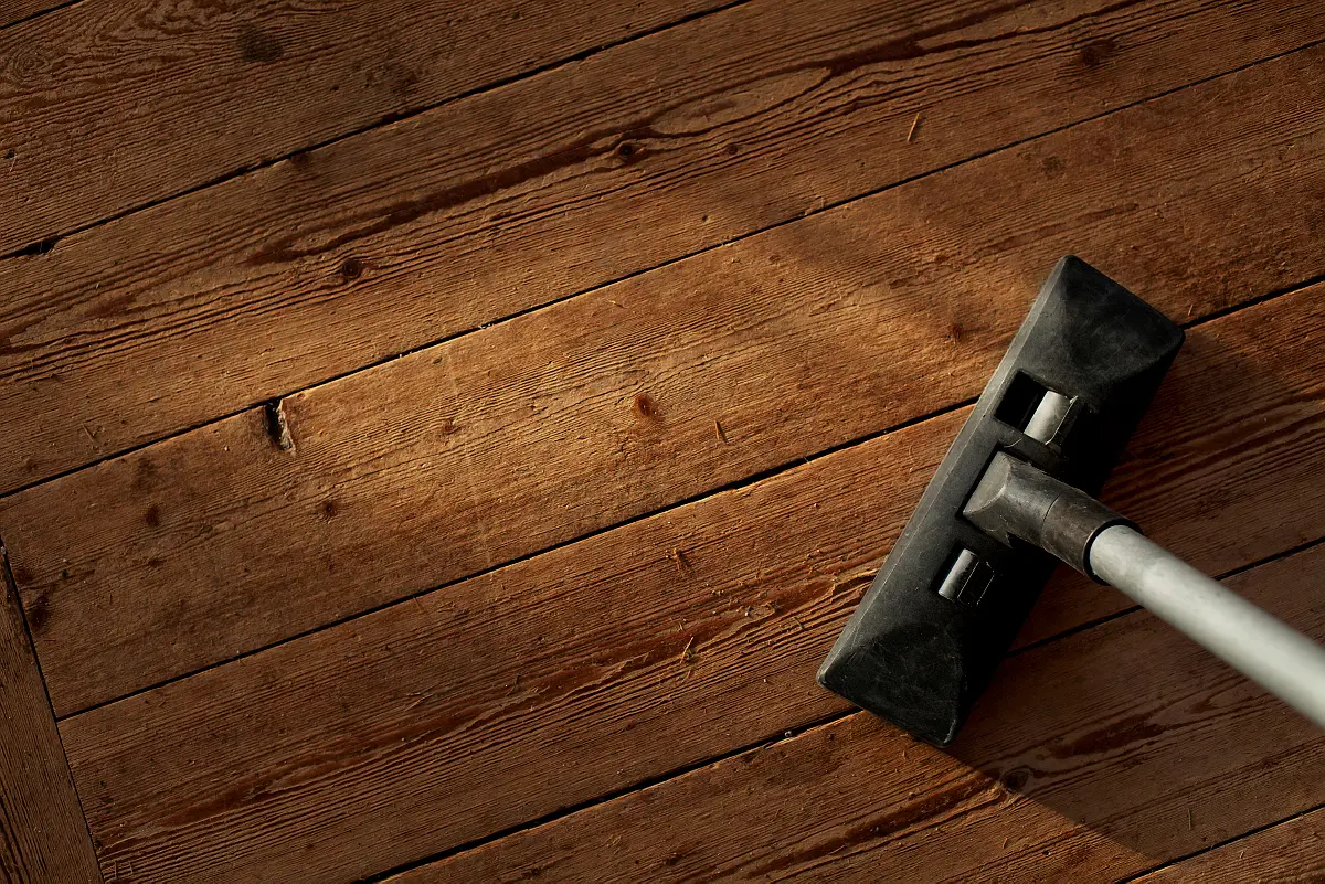 Ett svart dammsugarmunstycke fotat uppifrån på ett slitet trägolv.