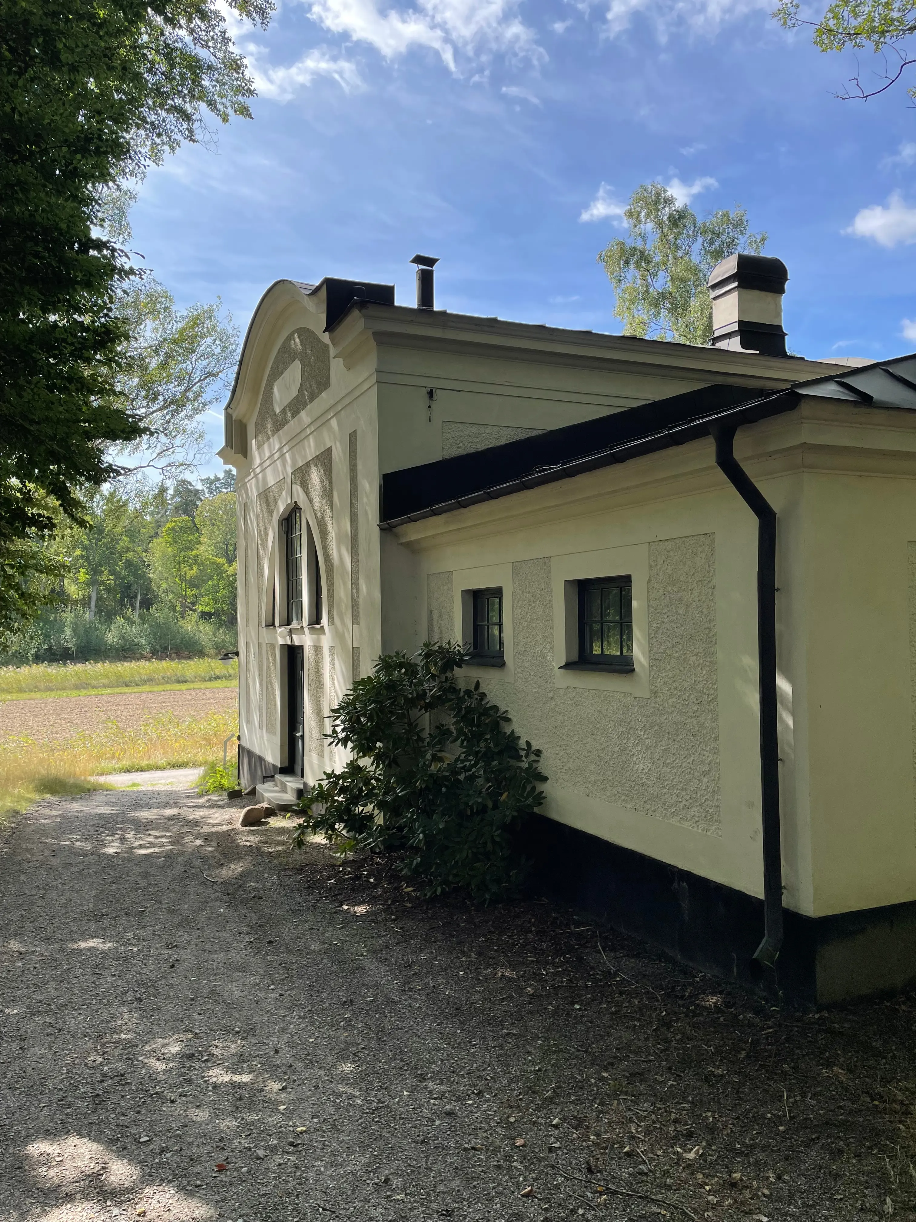 Ateljébyggnaden. Ett litet, vitputsat hus i enkel jugendstil. Sommar och grönska.