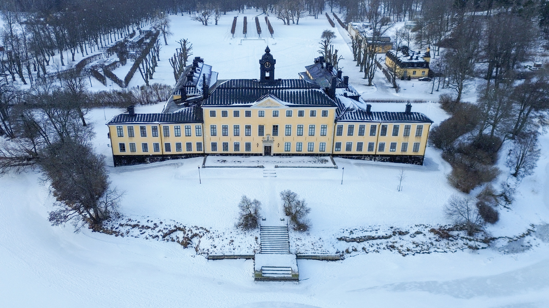 Drönarbild av Ulriksdals slott från vattnet. Framför slottet går en trappa ner till en brygga. Vinter och snö.