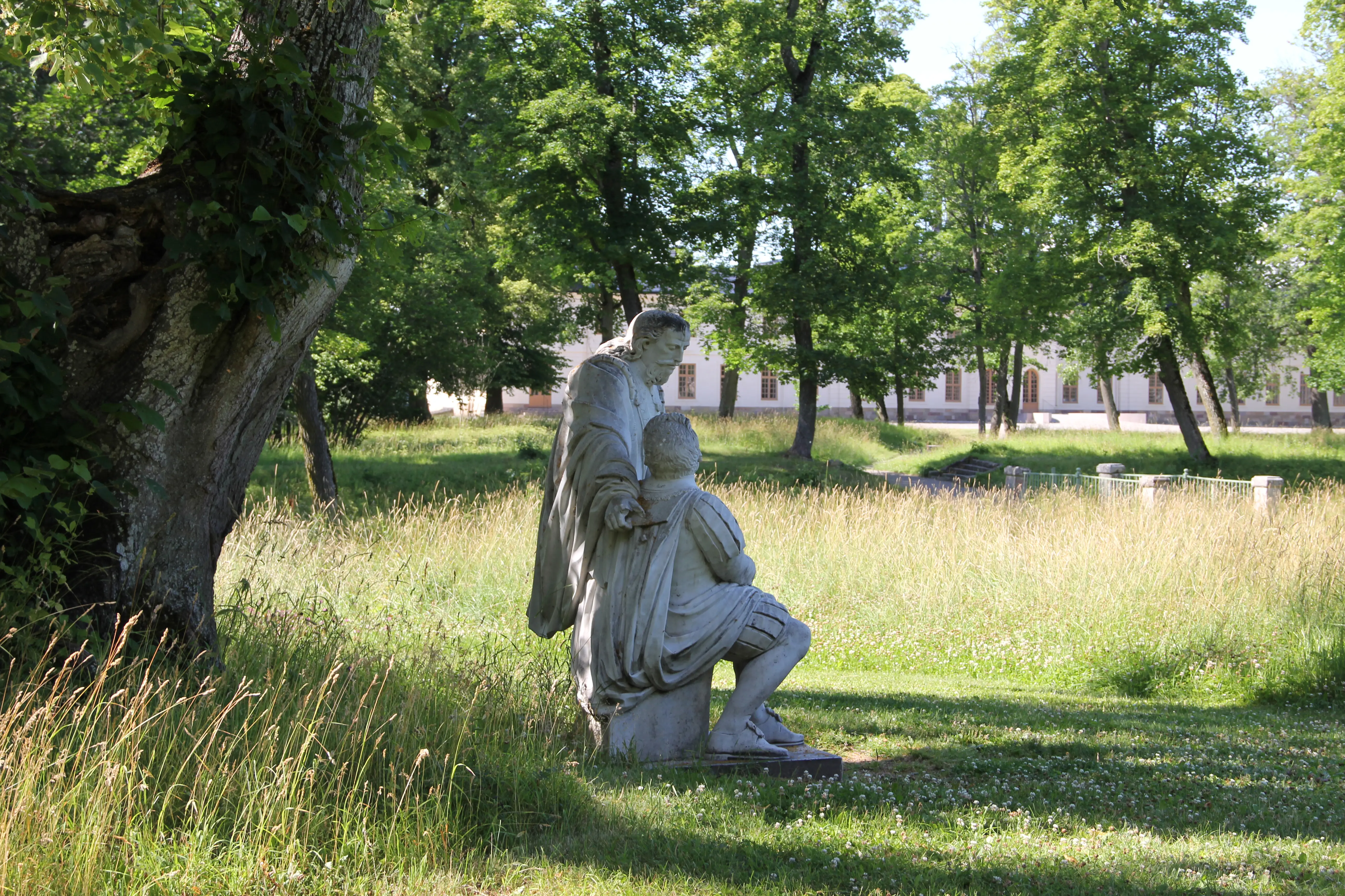 Skulptur föreställande Gustav II Adolf i samspråk med Axel Oxenstierna under Drottning Kristinas lind i Svartsjö slottspark. Sommar och grönska.