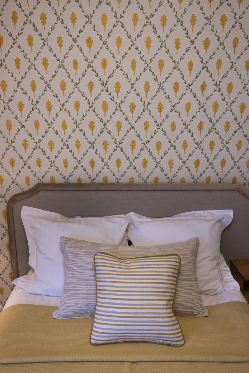 Bäddad gästsäng med dekorerad tapet i vitt, gult och grönt.