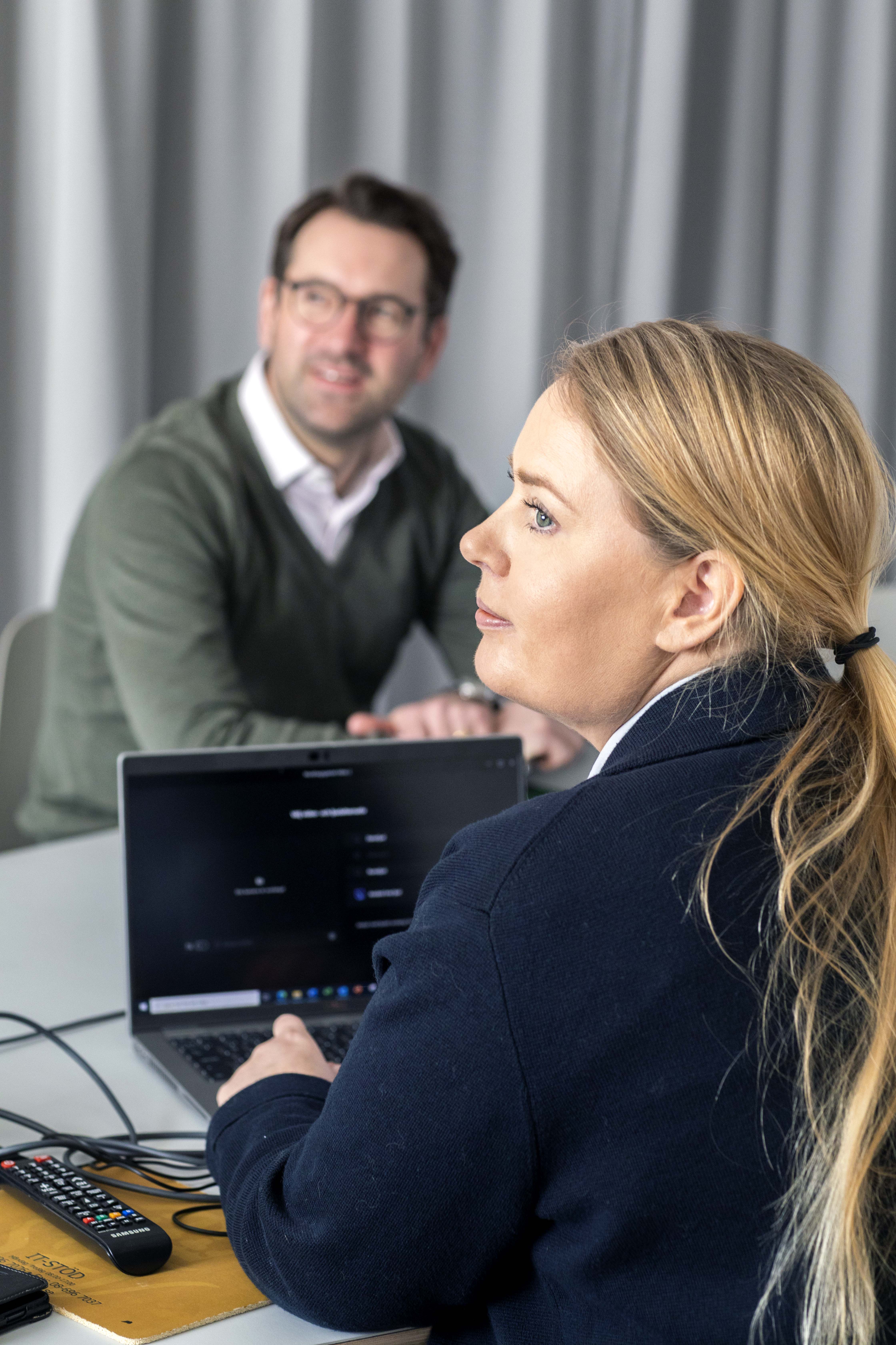 Två personer sitter i ett mötesrum med en laptop.