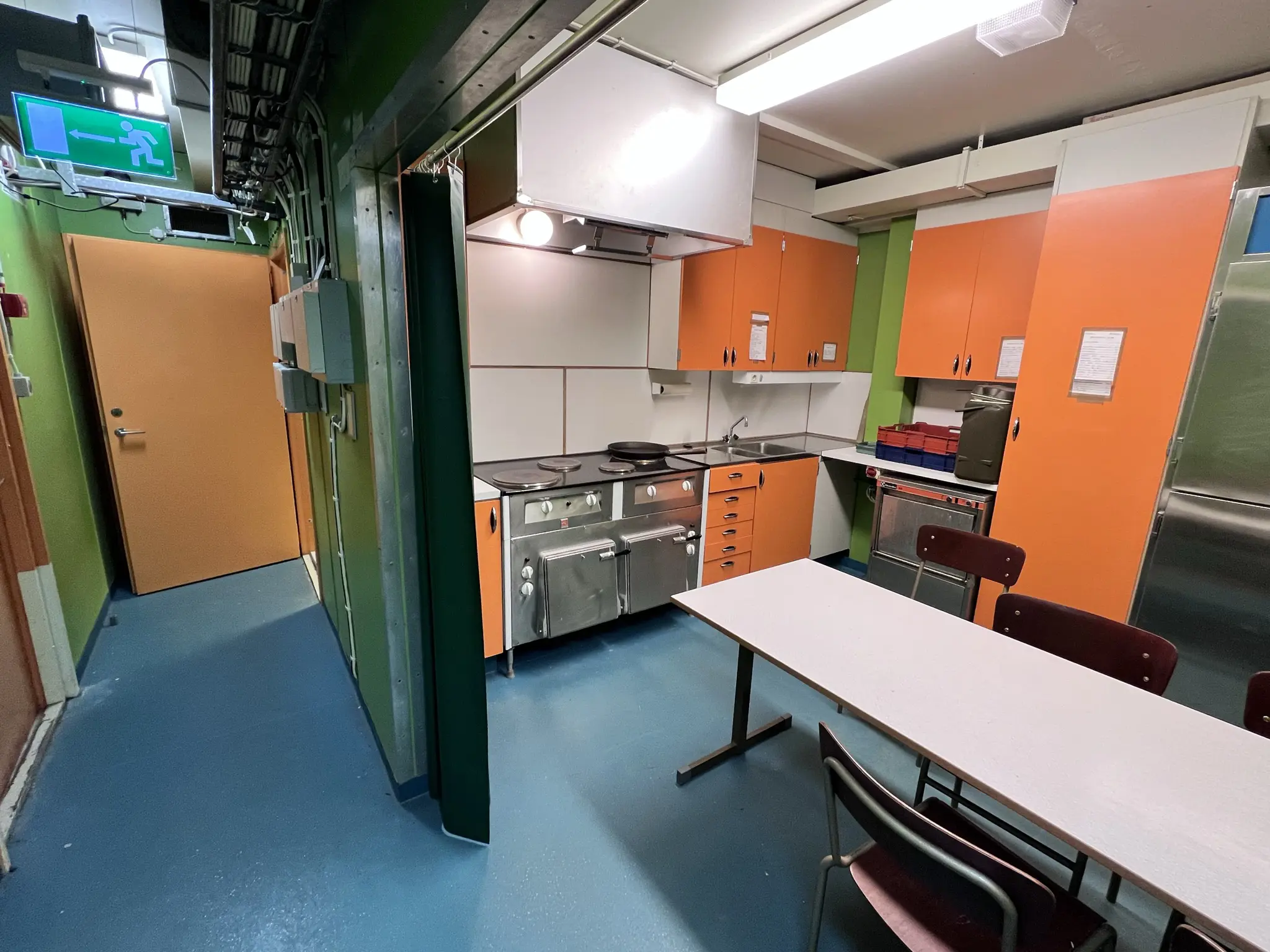Erstabatteriet, interiör. Ett enkelt inrett kök med diskbänk och vitvaror i rostfritt stål. Väggarna är gröna och alla skåpluckor och dörrar orangea.
