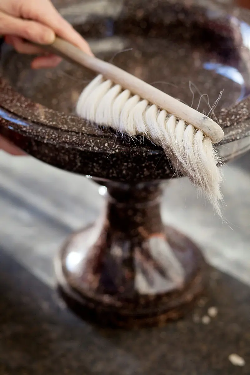 En borste med ljust träskaft används för att damma av en prydnadsskål.
