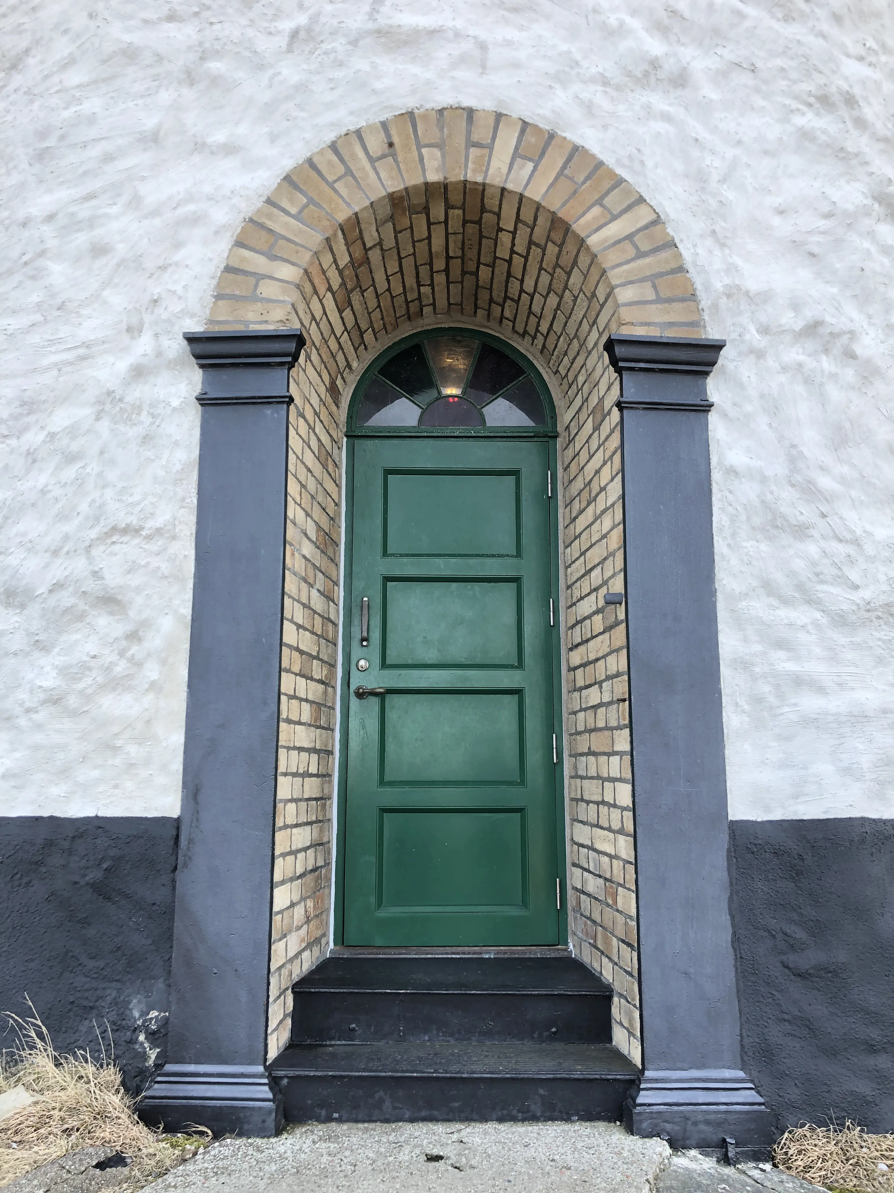 Porten till Landsorts fyr. En välvd portal av gult tegel i den vitputsade väggen. En liten trappa leder upp till en grön trädörr.