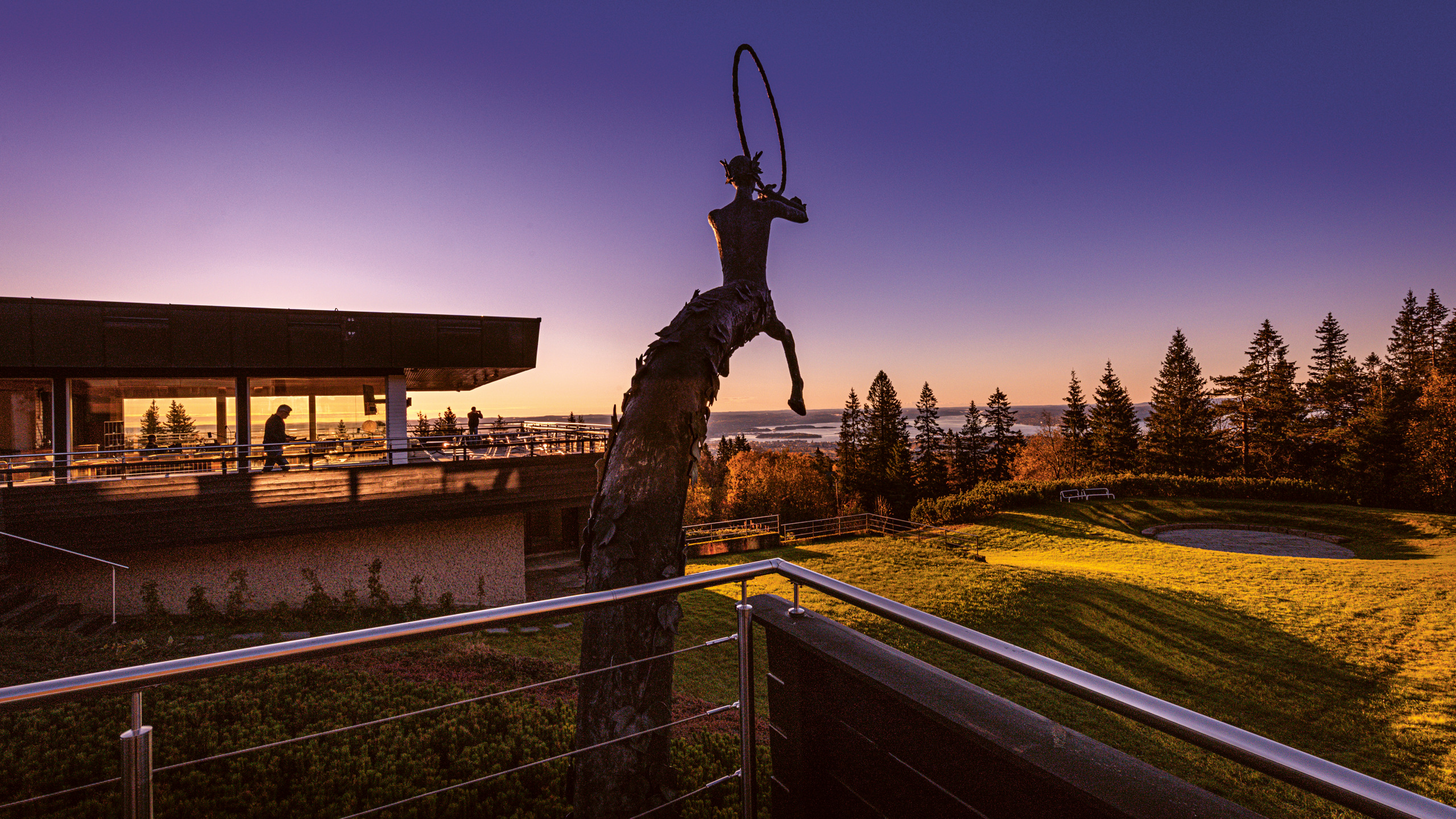 Voksenåsen. Modernistisk anläggning med stora terrasser och milsvid utsikt över ett fjord-landskap. I mitten av bilden står en brons-skulptur.