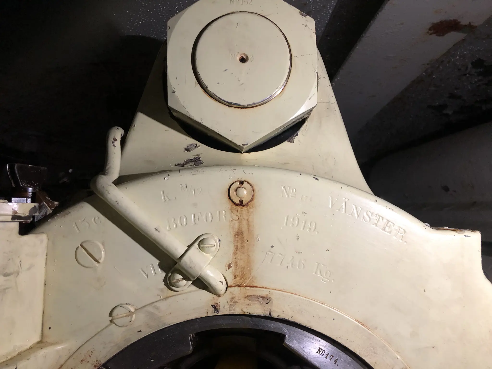 Närbild på laddningsmynning av en kanon. Metall, sladdar och skruvar målat i beige. Stämplat i metallen kring öppningen "15 cm K m/12 nr 174 Vänster Bofors 1919 vikt 7746 kg".