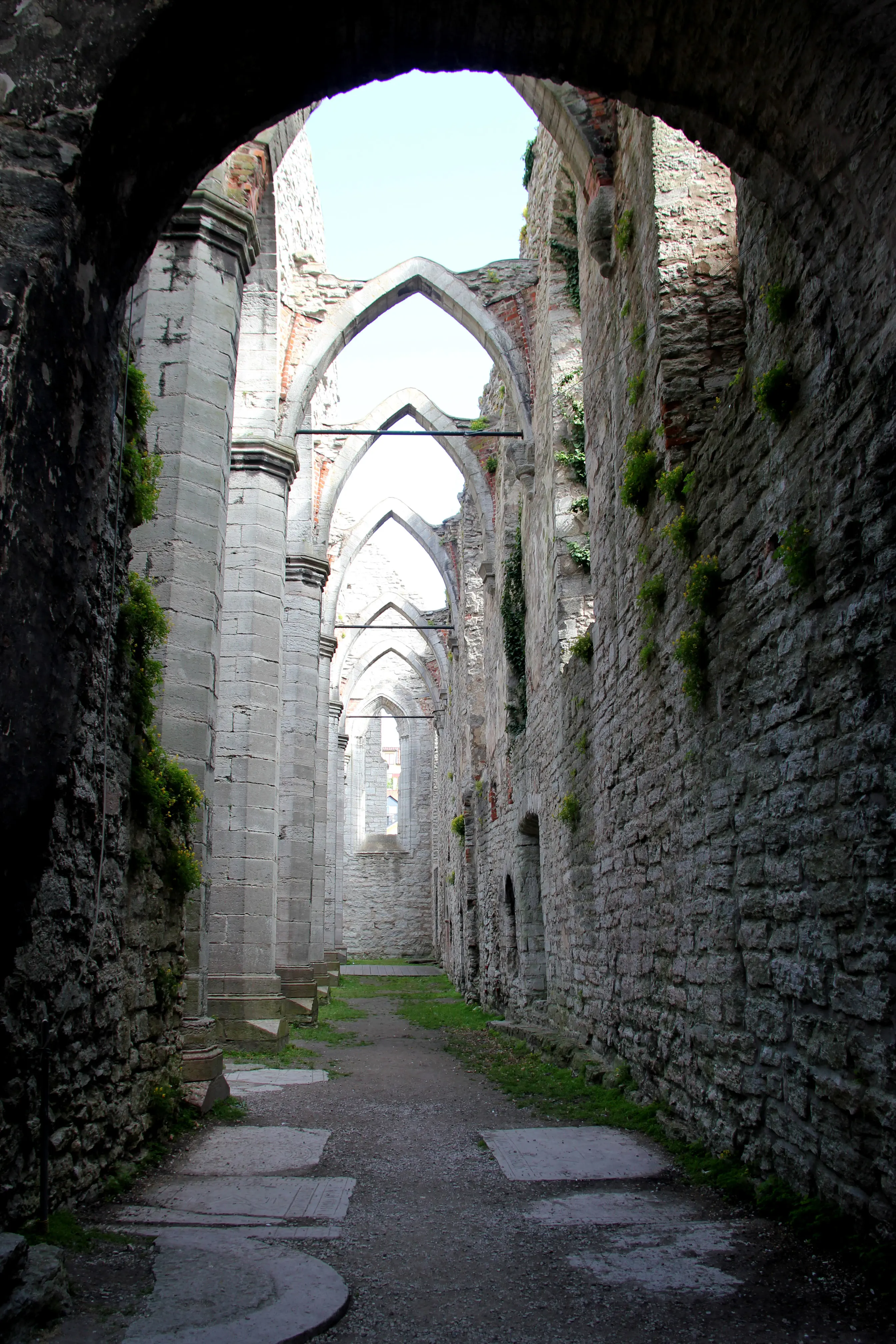 Interiör av kyrkoruin med höga valvbågar mot blå himmel.