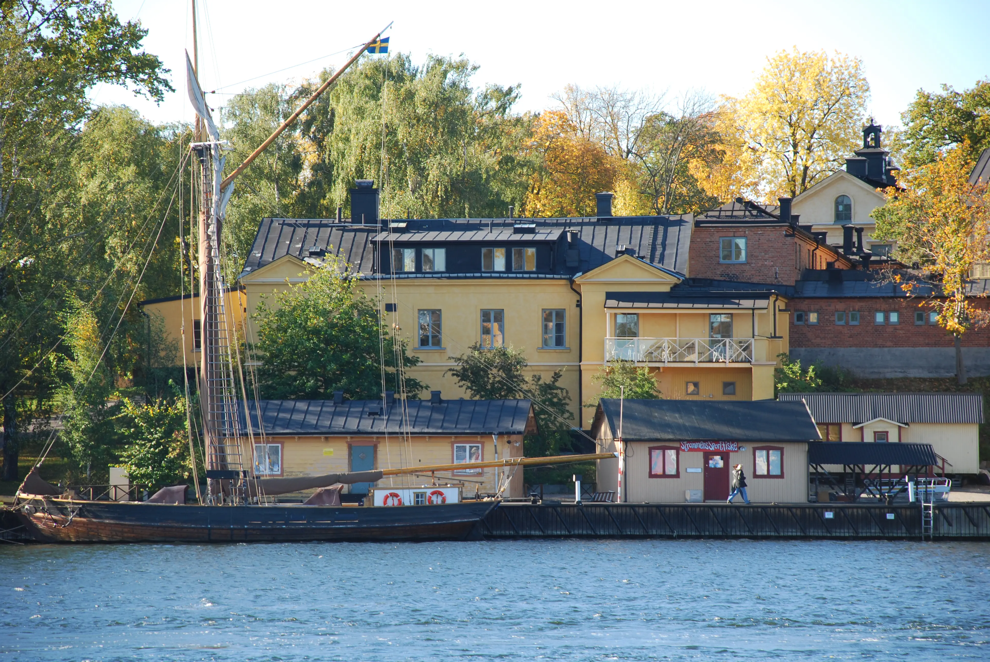 Gamla badhuset på Skeppsholmen sett över vattnet, från Djurgården. Gulputsad byggnad med tak-kupor och balkong.