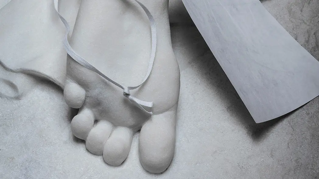 Närbild på en fot på vit marmorstaty. ett band med en tom etikett hänger på foten.