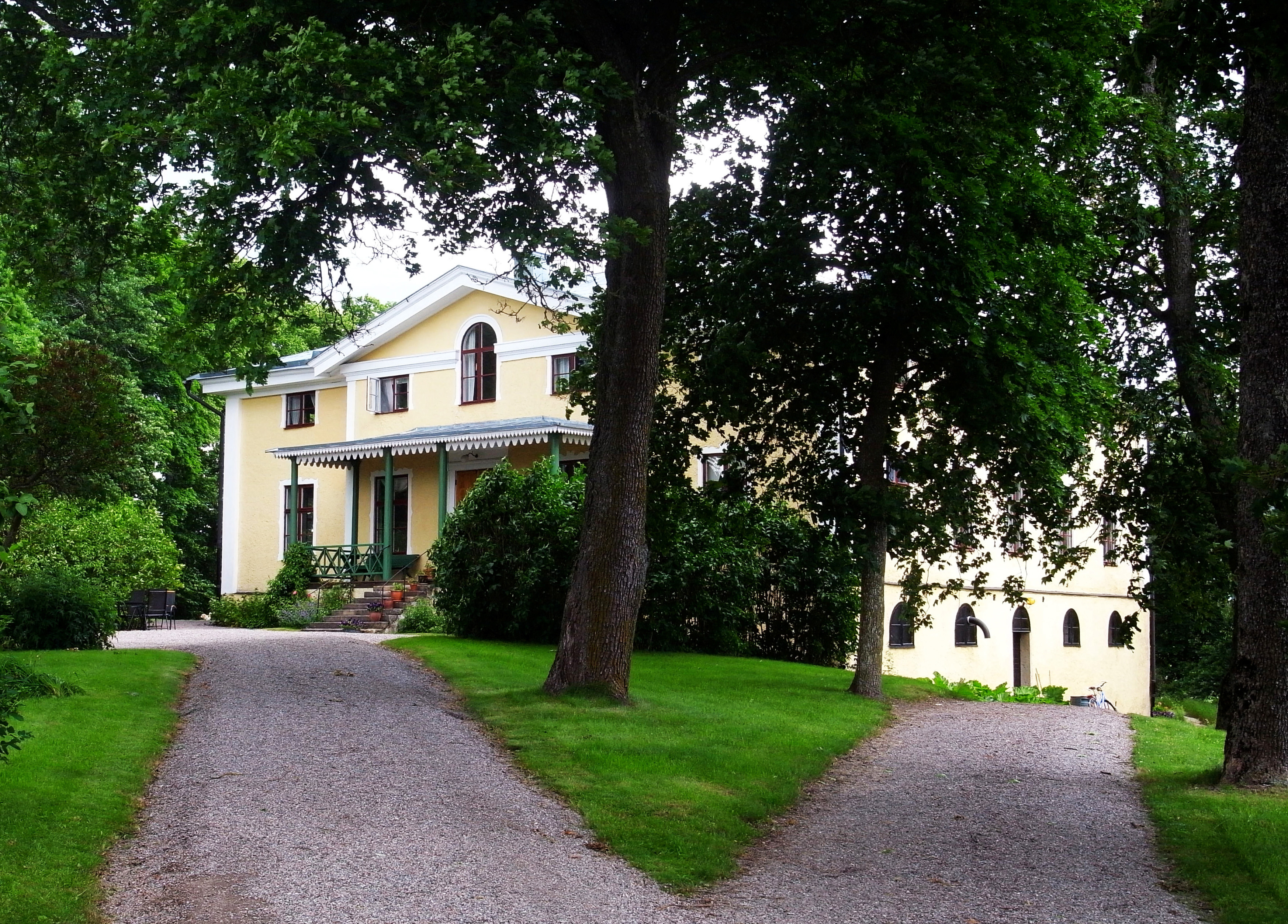 Landsberga översteboställe. Ett ljusgult pampigt souterränghus med vita knutar och ljusgrått tak. Sommar och grönska.