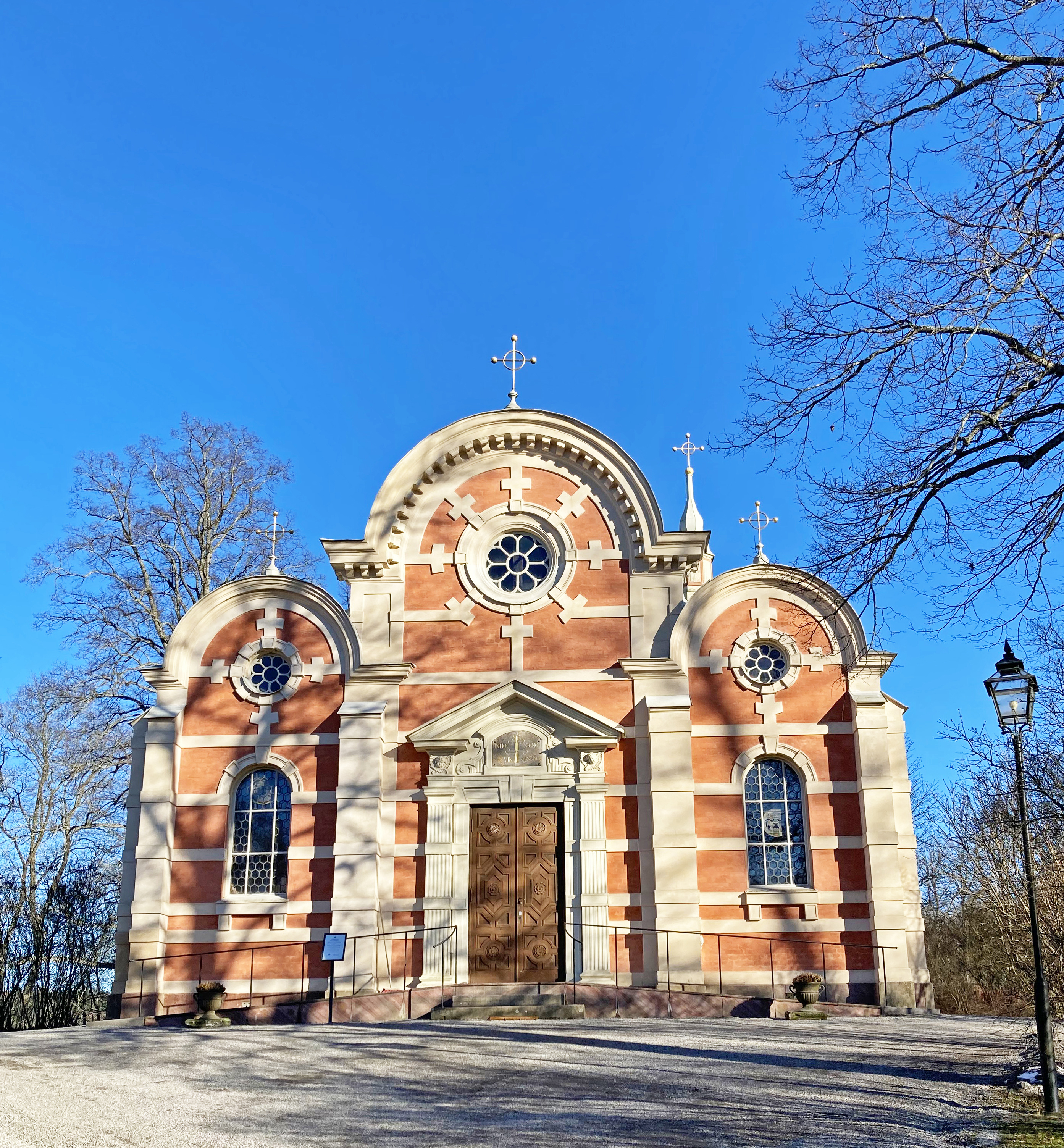 Ulriksdals slottskapell. Rosa byggnad med vita inramningar. Gavlarna är rundade ovanför enkla rosett-fönster. Tidig vår.
