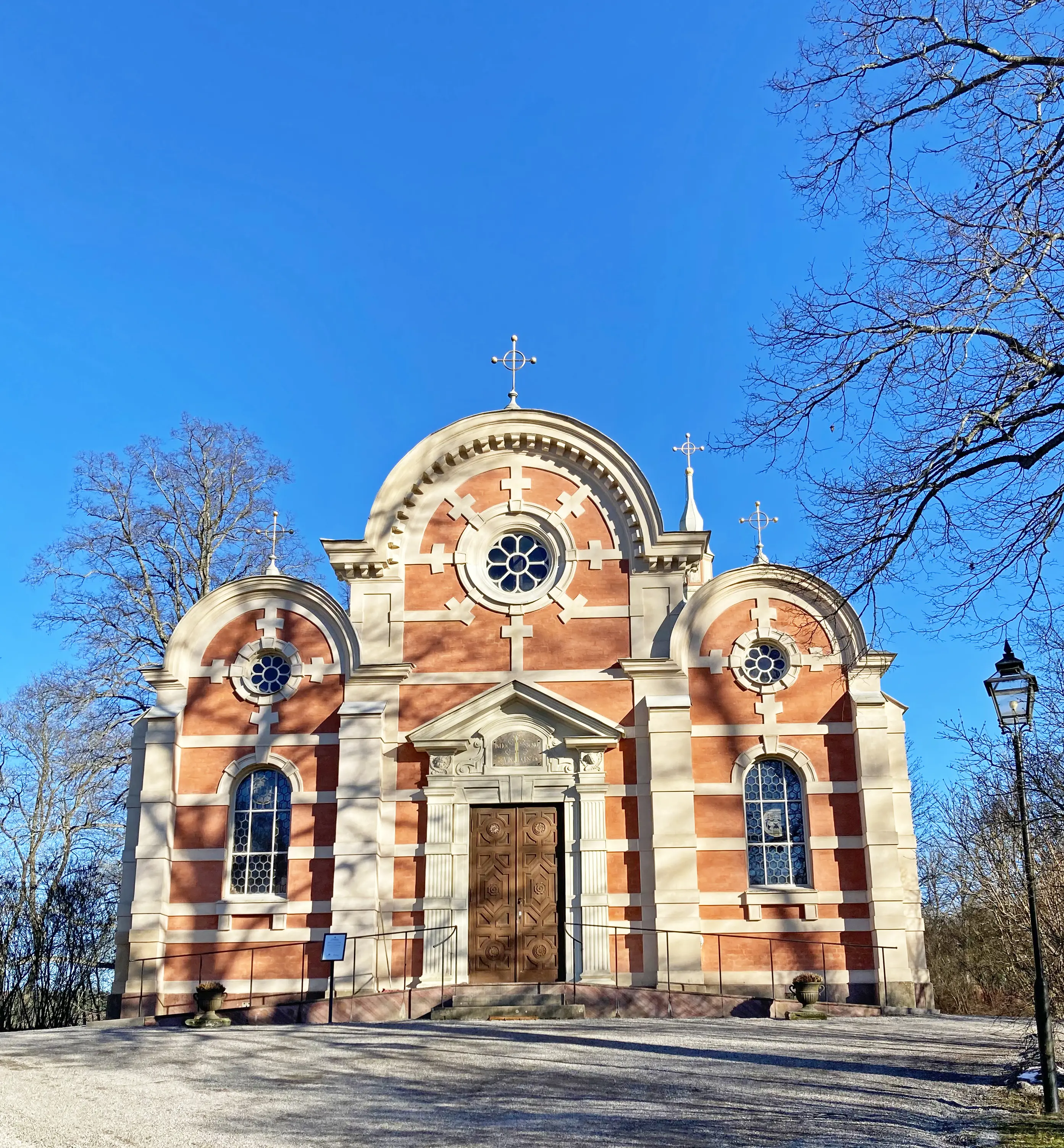 Ulriksdals slottskapell. Rosa byggnad med vita inramningar. Gavlarna är rundade ovanför enkla rosett-fönster. Tidig vår.
