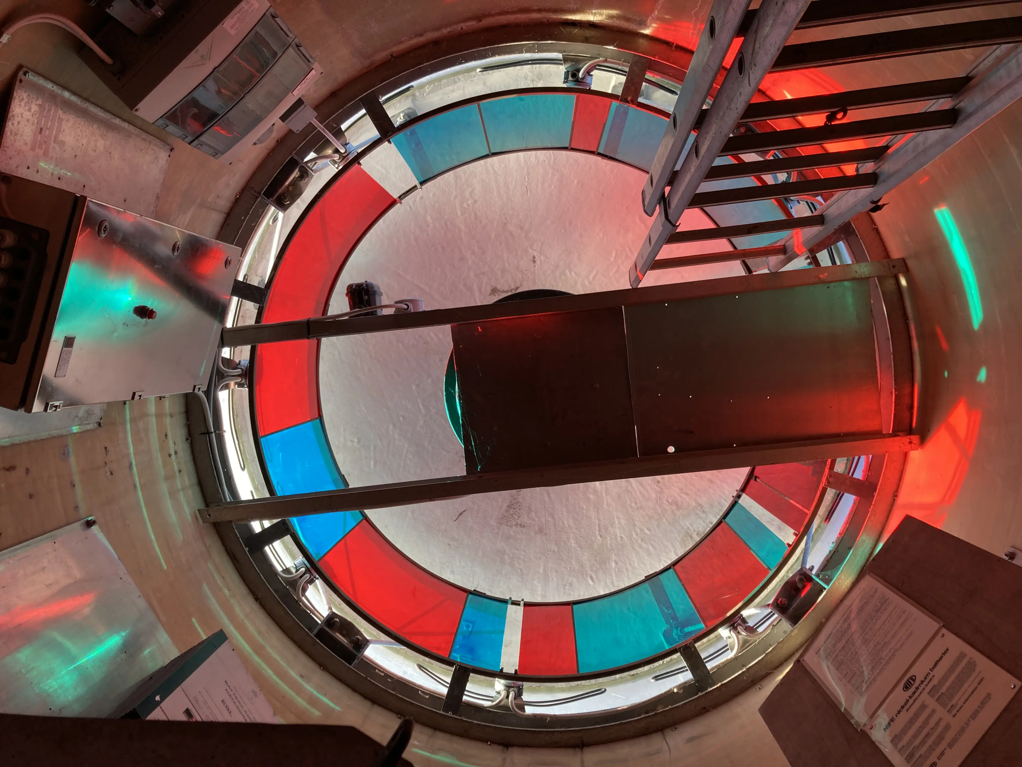 Godnatts fästning. Fyr-lanterninen sett underifrån. En rund konstruktion med rött och blått glas.