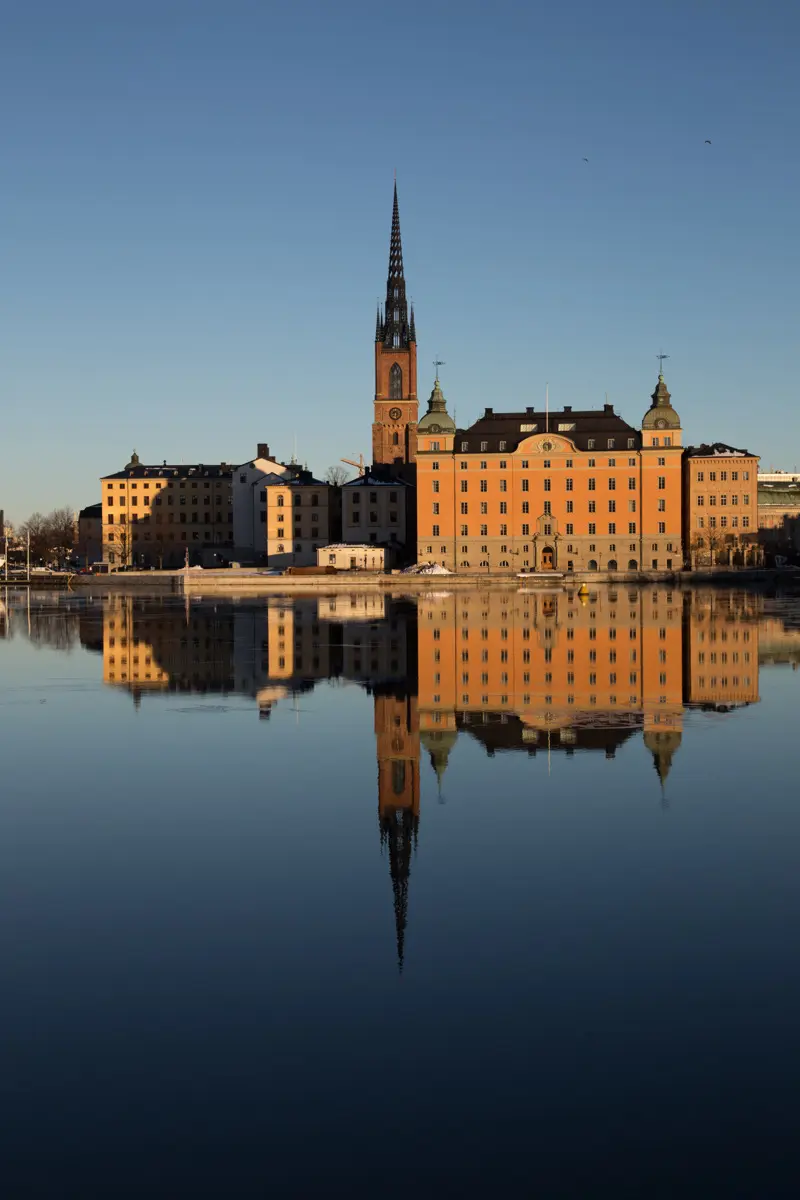 Riddarholmen sedd från Söder. Riddarholmskyrkans torn och andra byggnader speglas i Riddarfjärdens vatten.