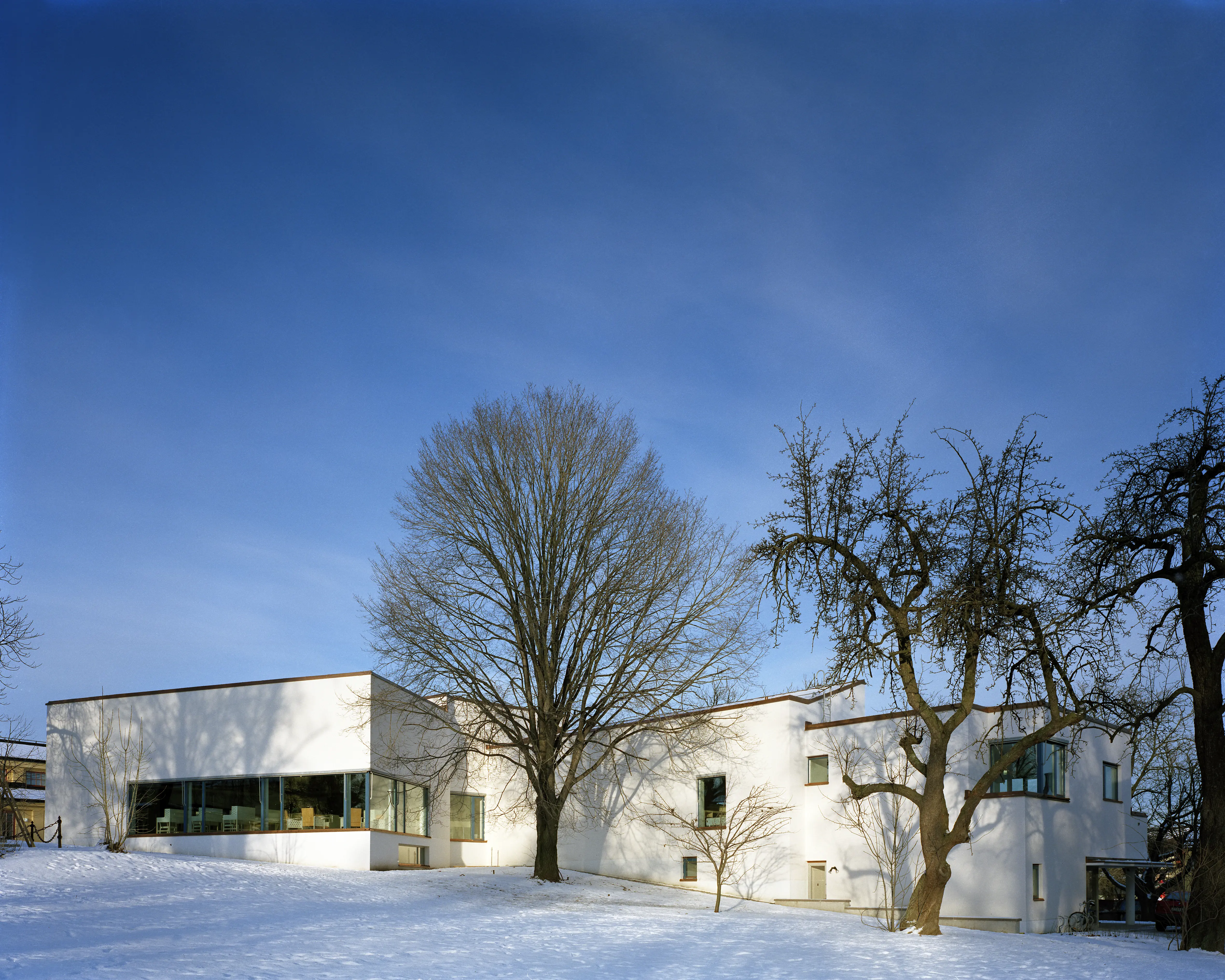 Arkitektur- och design-centrum, flygeln. En vit, modernistisk byggnad. Vinter och snö. Några träd avtecknar sig mot fasaden och himlen