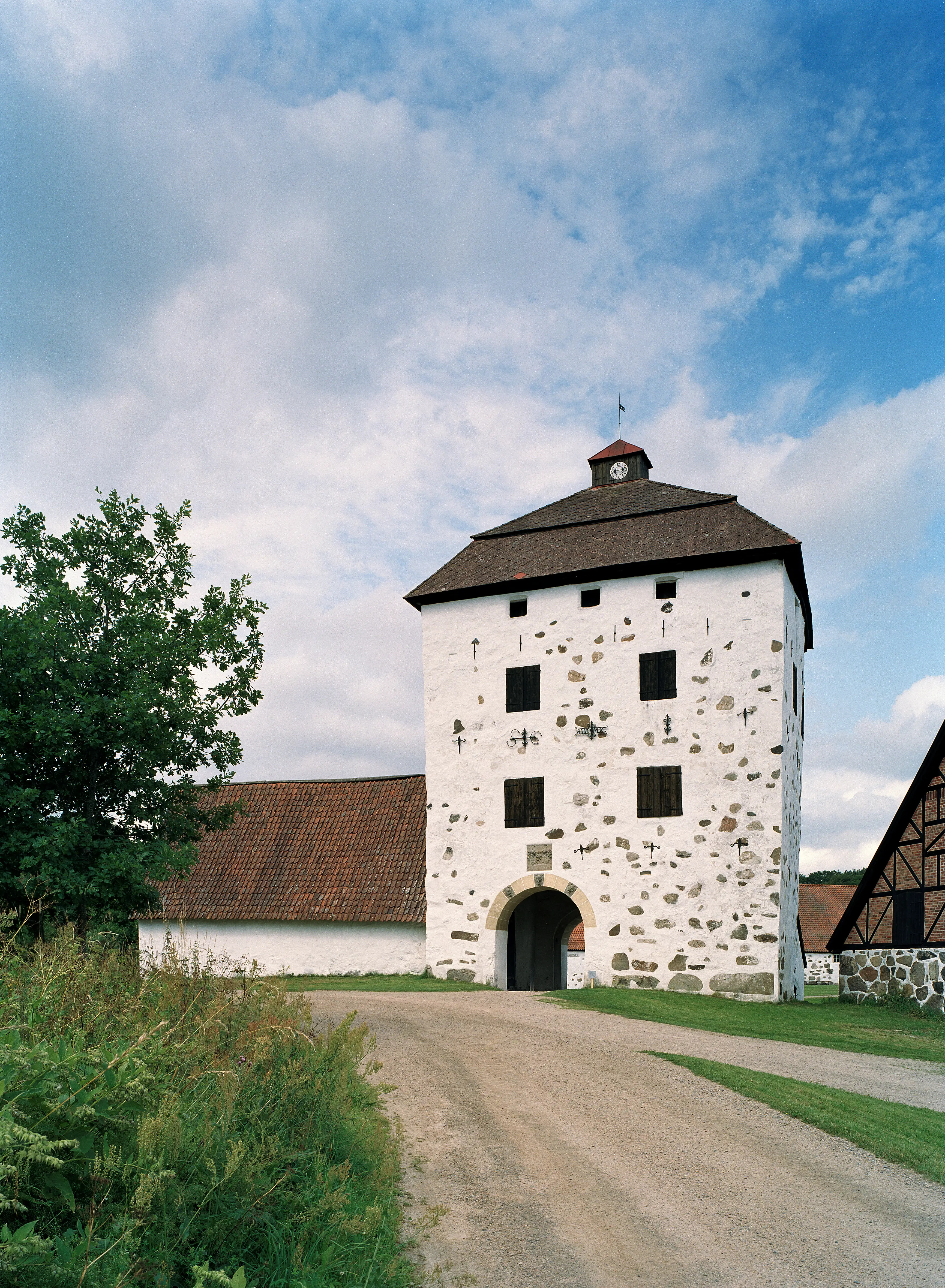 Tornbyggnad vid Hovdala slott. En vitputsad stenbyggnad med säteritak och olikformade ankarslut. Ett valv leder in till gårdsplanen.