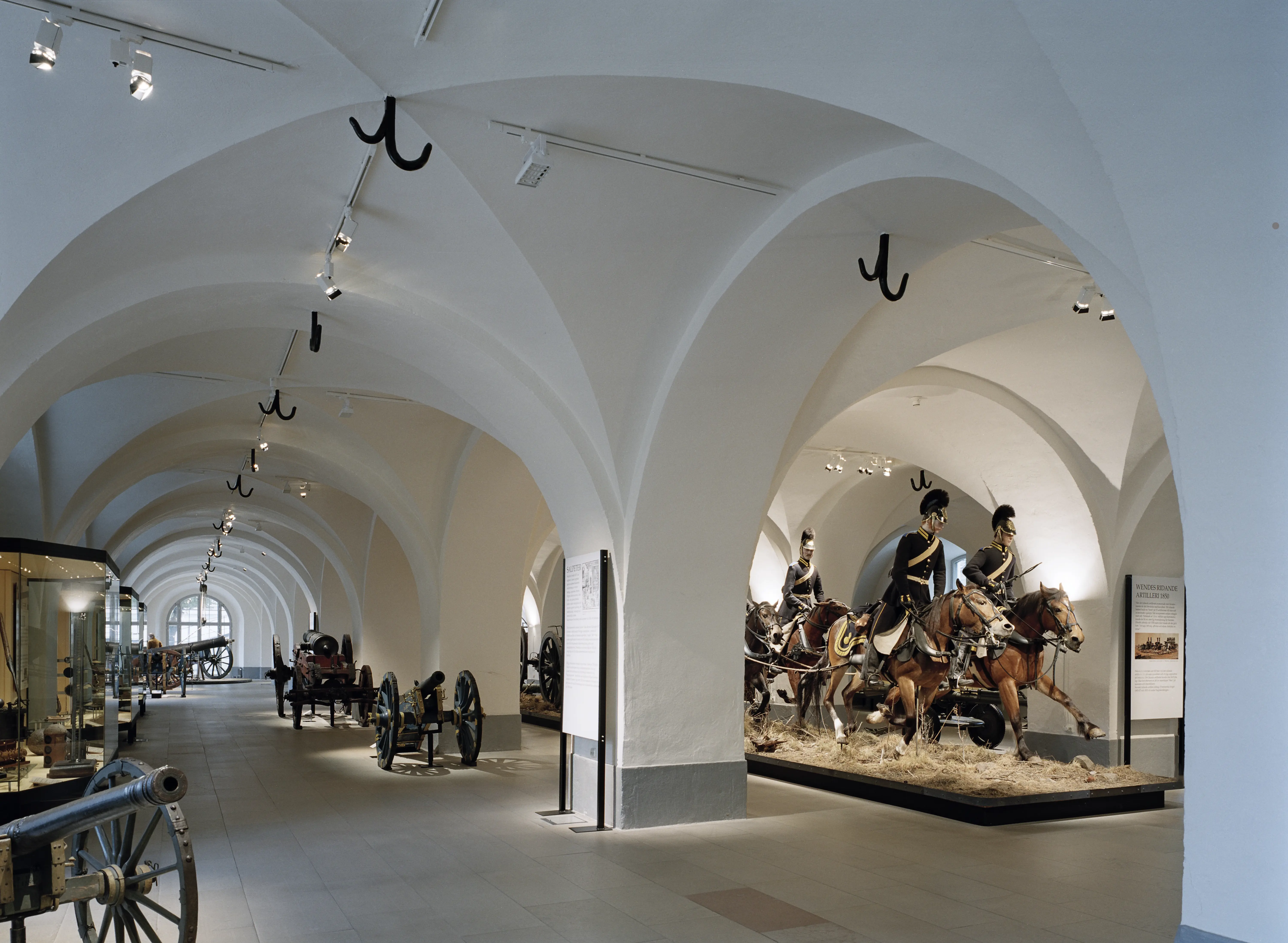 Interiör, armémuseum i Stockholm. Utställnings-rum med kryss-valv och pelare. Där står kanoner av olika storlek.