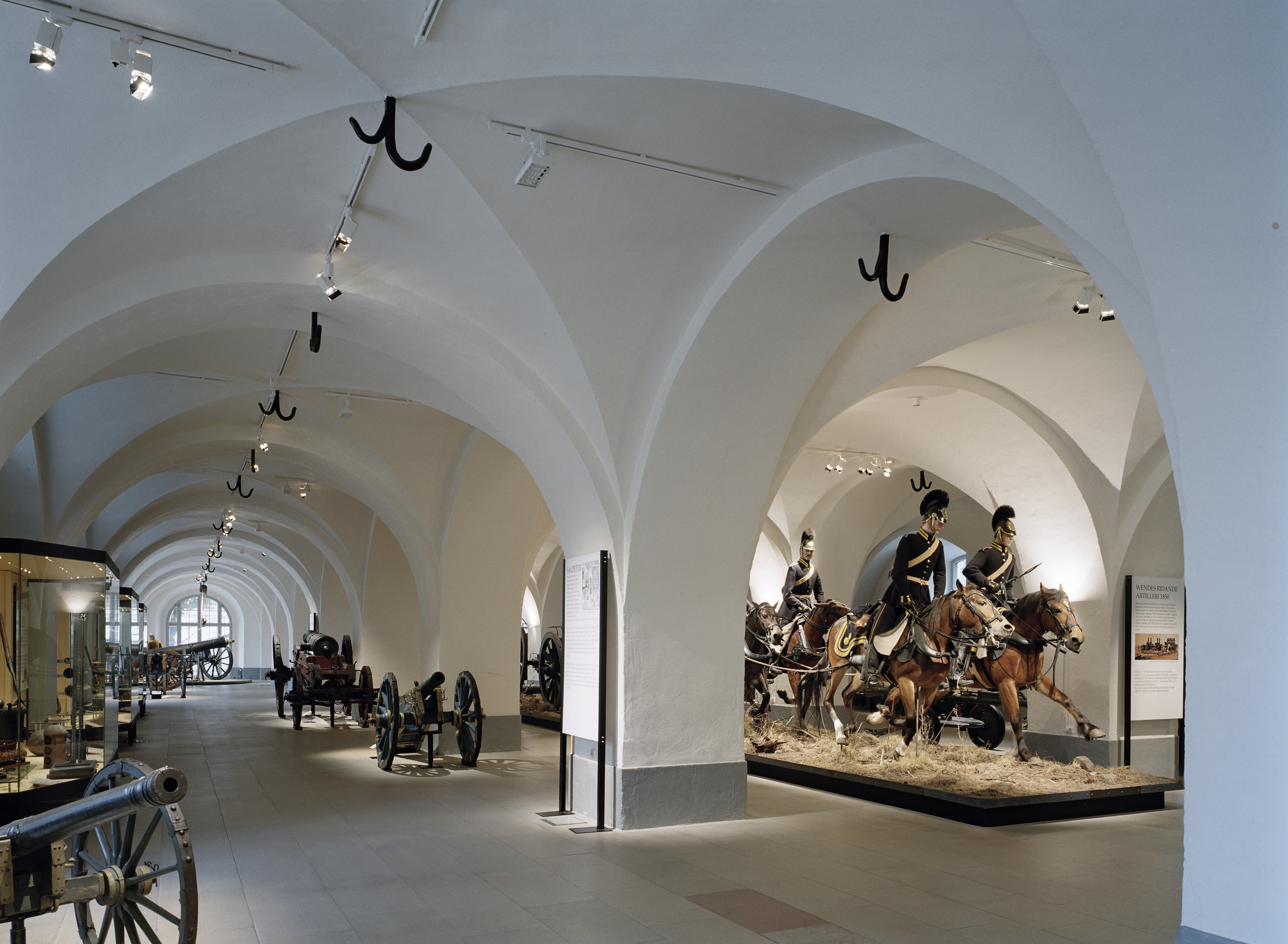 Interiör, armémuseum i Stockholm. Utställnings-rum med kryss-valv och pelare. Där står kanoner av olika storlek.