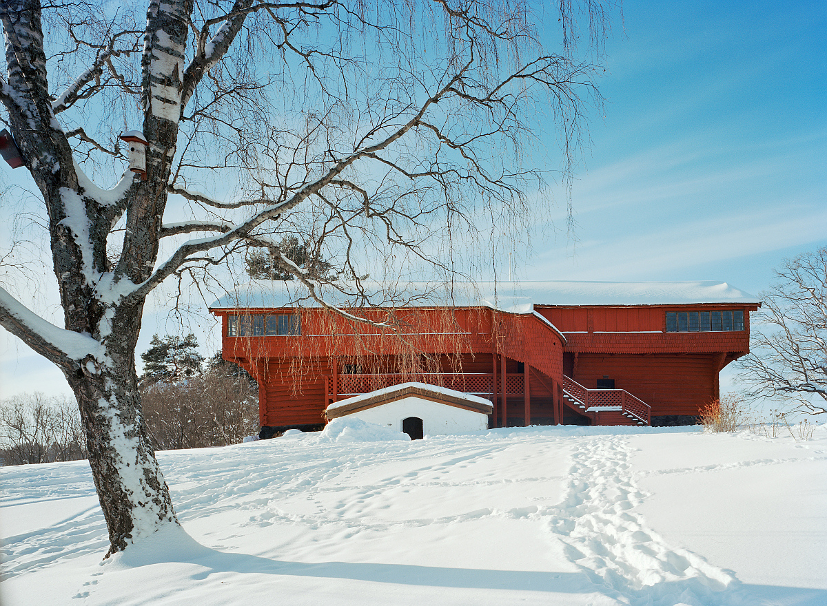 Det röda Ornäsloftet ligger uppe på en höjd mot en blå himmel och snötäckt mark.