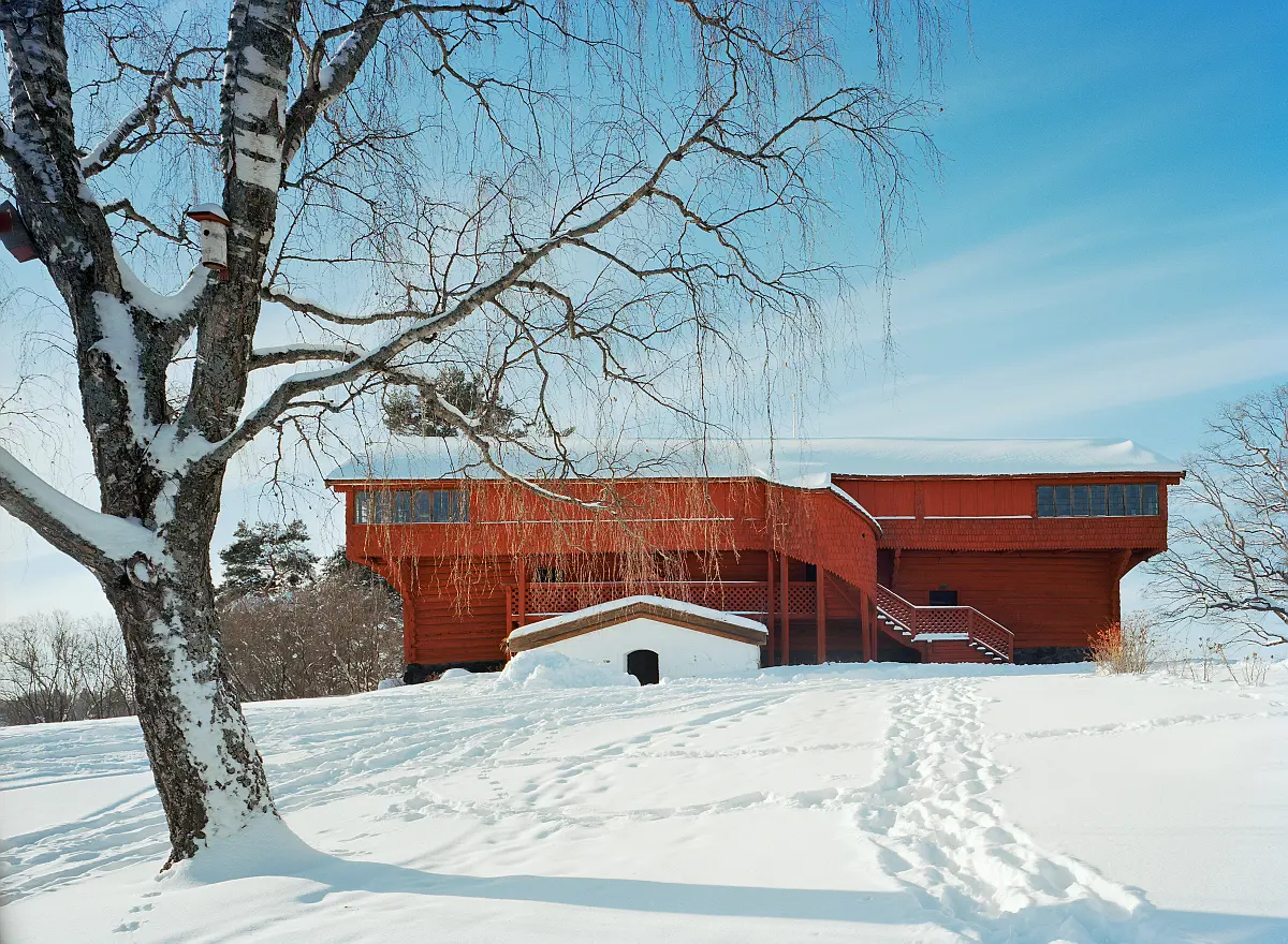 Det röda Ornäsloftet ligger uppe på en höjd mot en blå himmel och snötäckt mark.