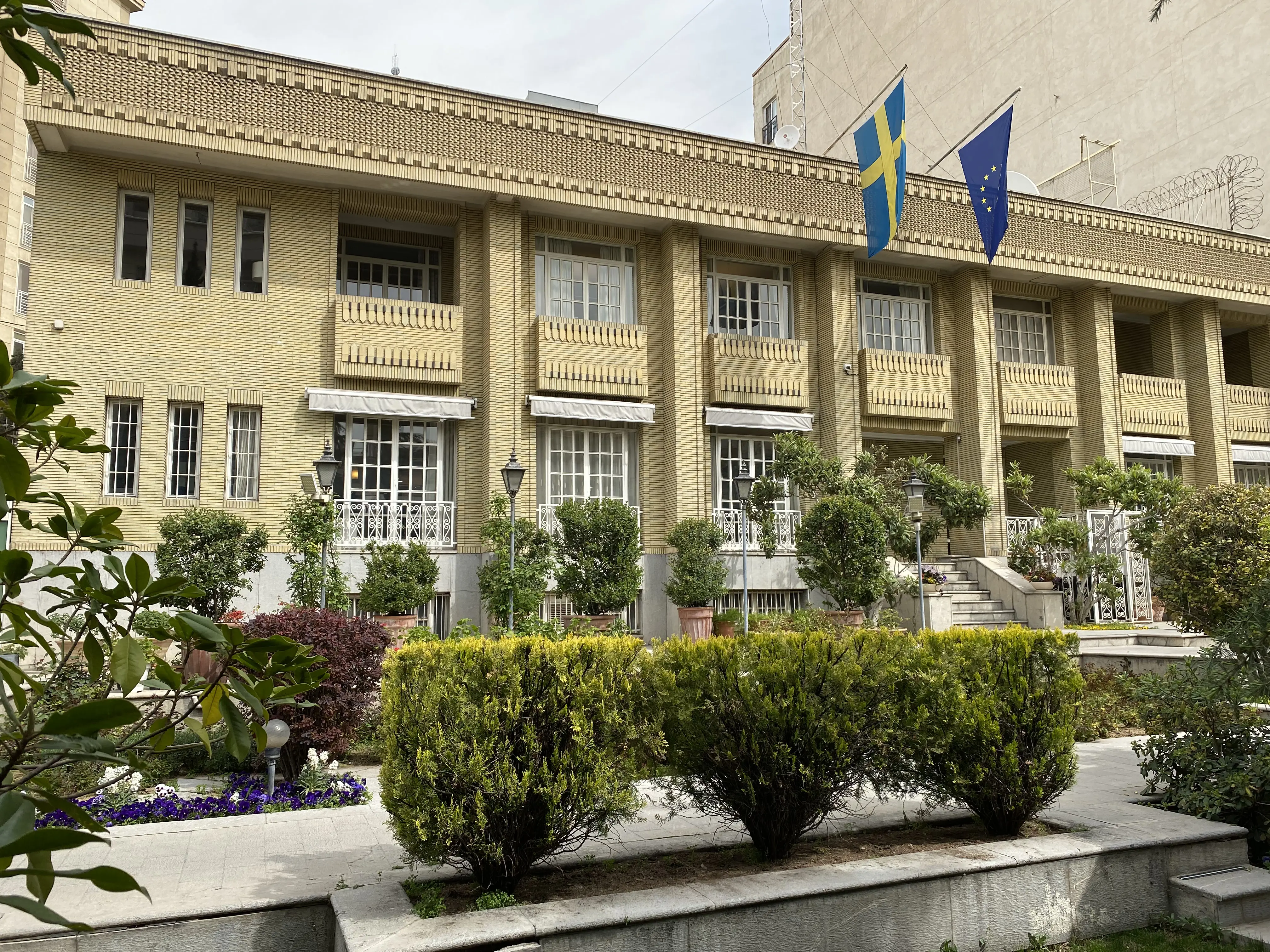 Ambassaden i Teheran, entréfasad. Framför byggnader löper låga stenterasser med buskar och blommor.