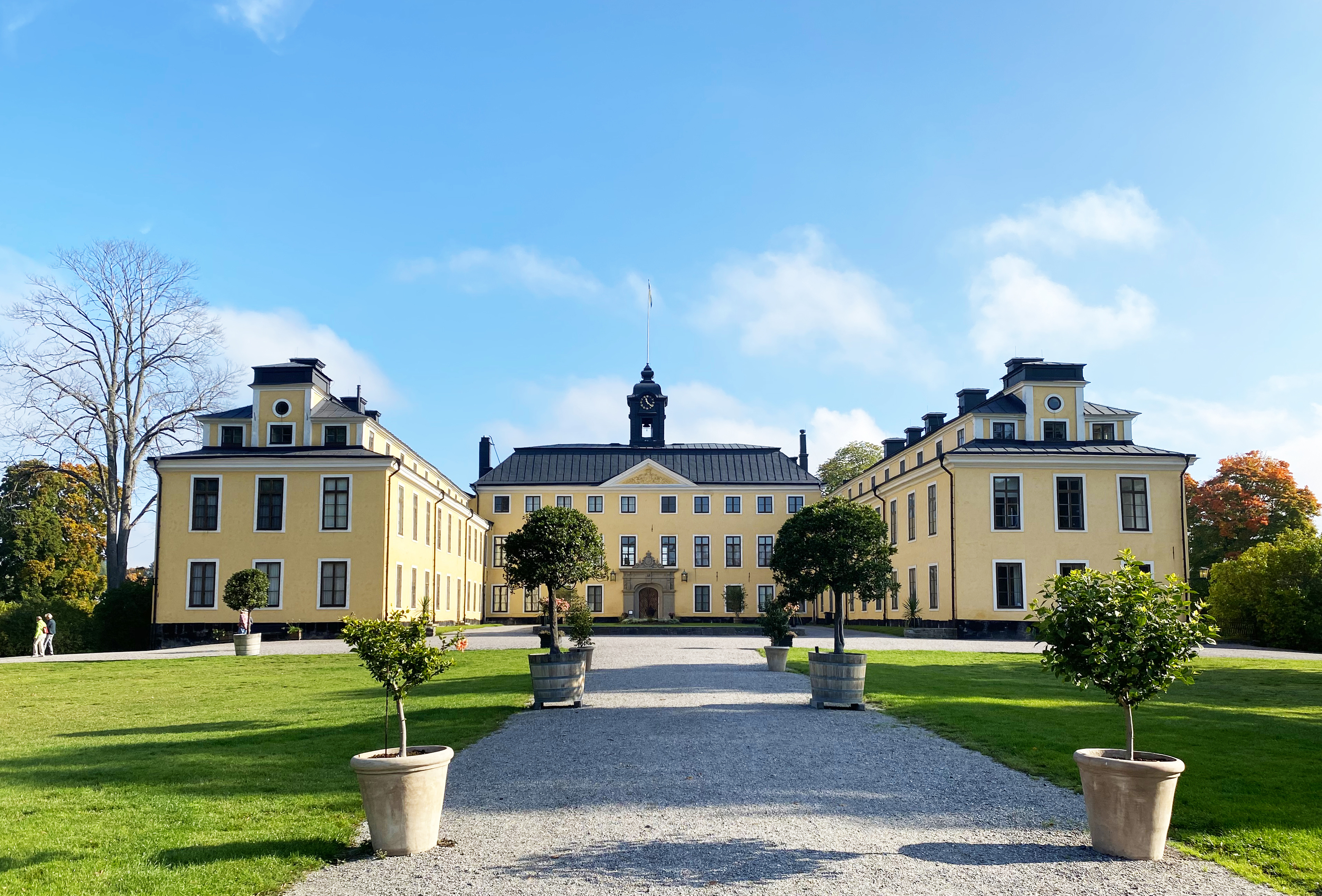 Ulriksdals slott. Ett ljusgult slott i tre våningar med flyglar. Det svarta taket har en lanternin. Tidig, solig höst.