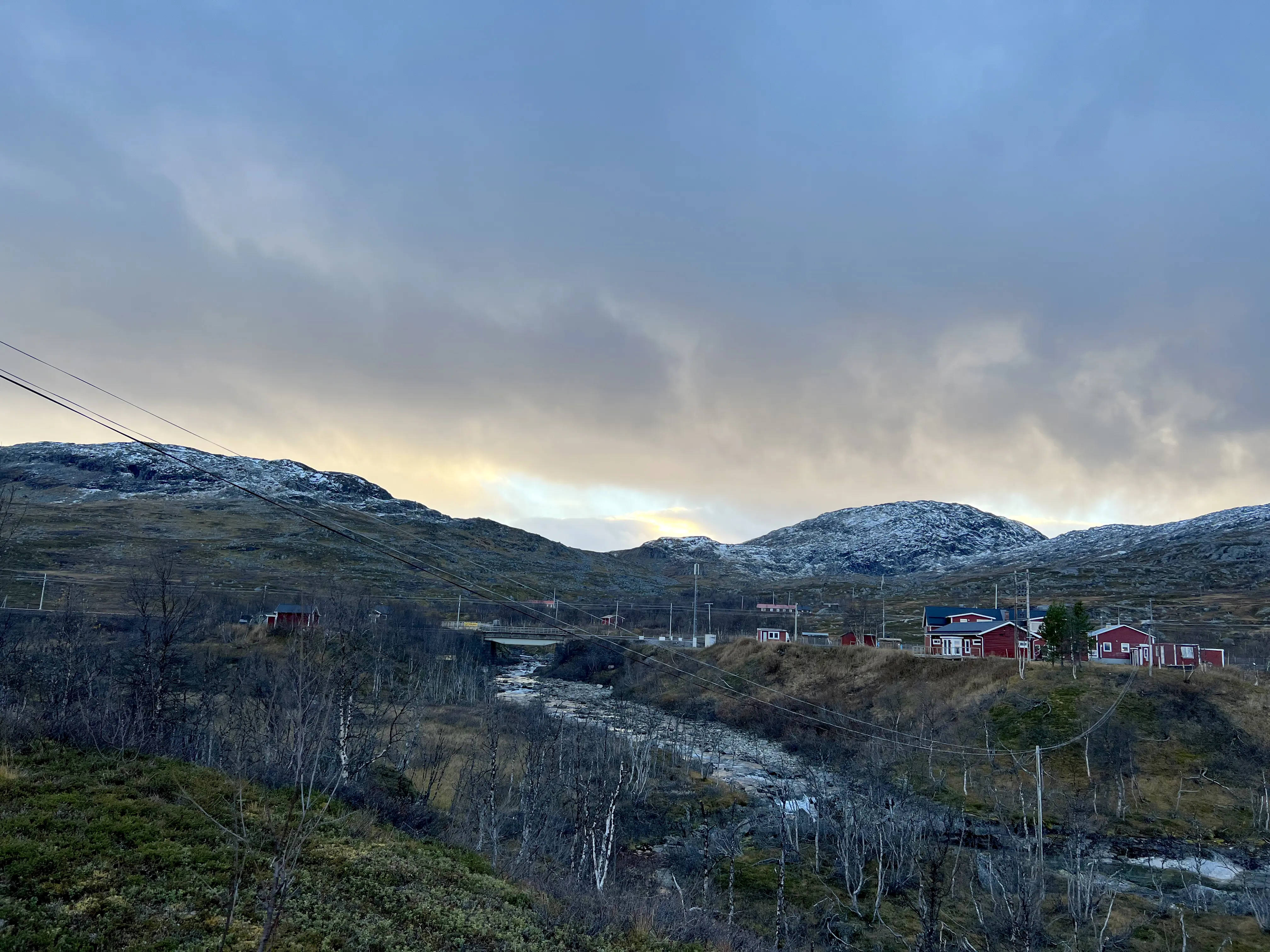En vy över ett vackert fjällandskap med en å som rinner i mitten och röda hus längs med kanterna.
