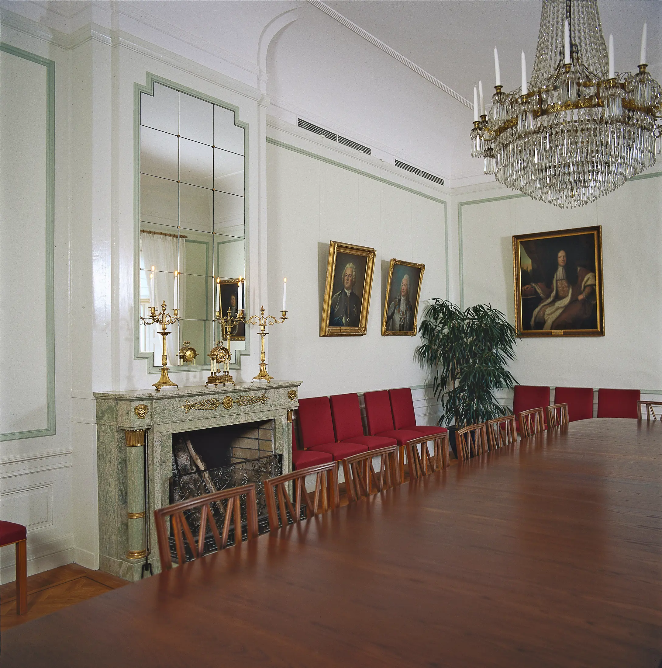 Interiör, residenset i Nyköping. Salong med utsmyckad öppen spis och kristall-krona. Ovanför spisen sitter en inbyggd spegel. Ett stort mahogny-färgat bord tar upp en stor del av rummet