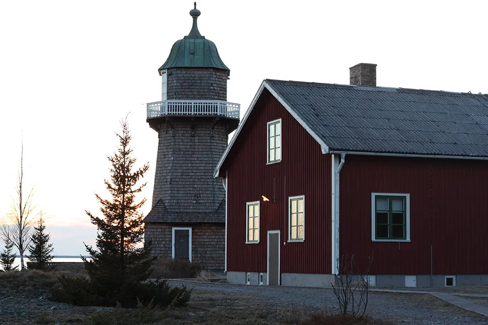 Berguddens fyrplats. Fyrtornet har en kopparklädd, toppig, tak-kupol. Fyrvaktarbostaden är rödmålad med vita snickerier. Kväll.