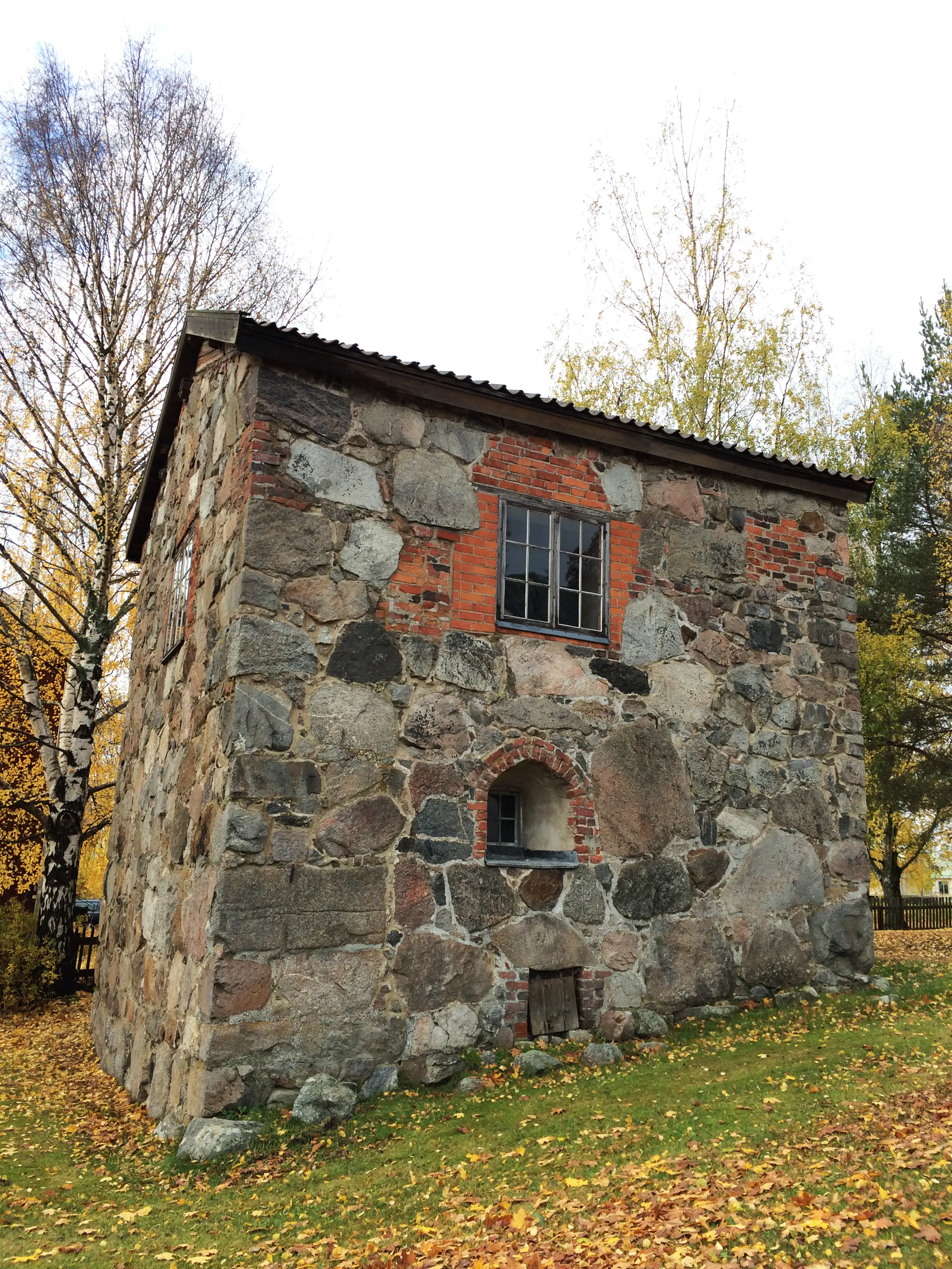 Forsa gillestuga. En medeltida byggnad i grå sten. Två fönster och en källarlucka är infattade i tegel. Höst och gula löv.