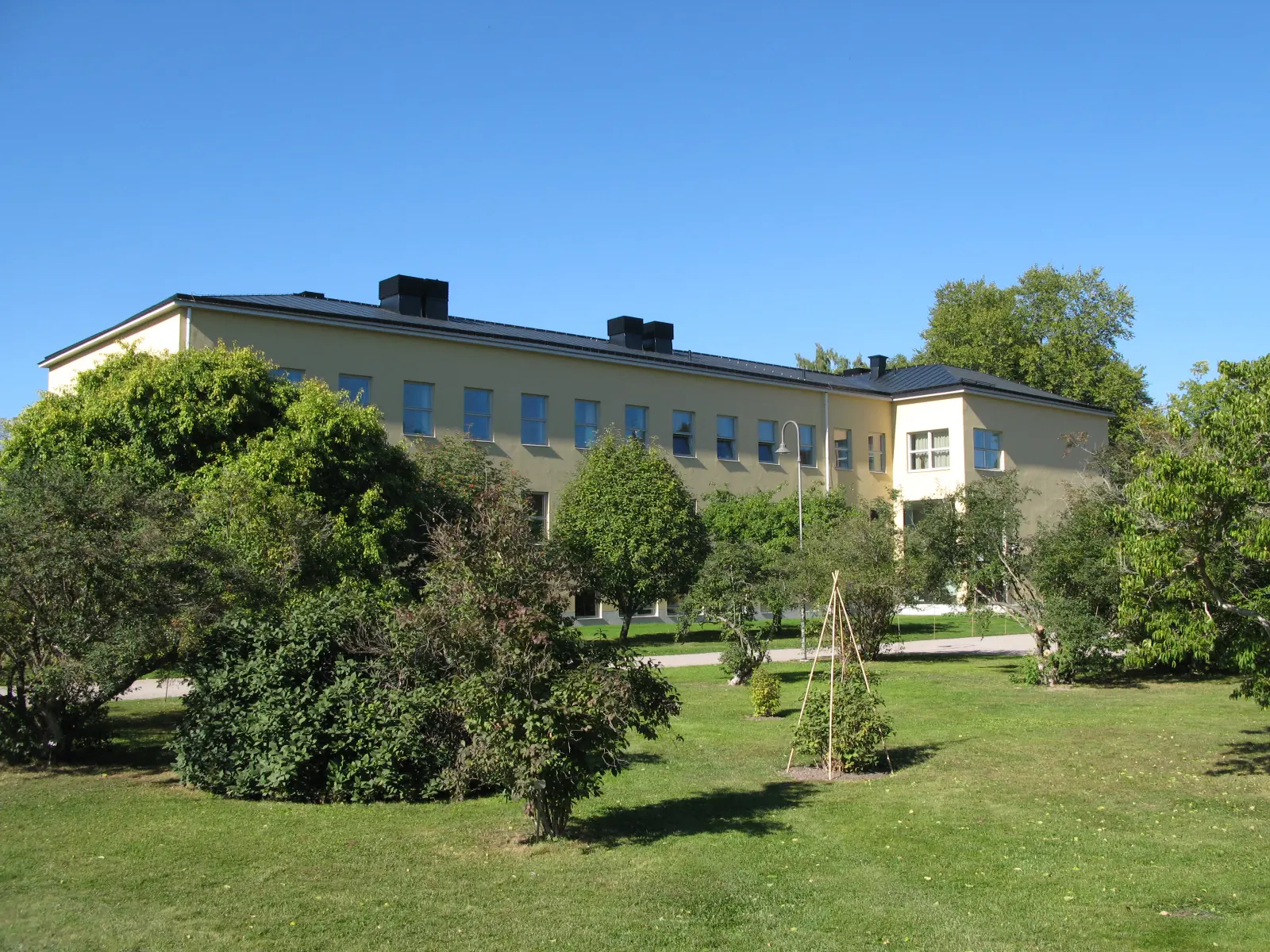 Institutionsbyggnad i botaniska trädgården. Gulputsat tvåvåningshus i funkisstil. Sommar och grönska.
