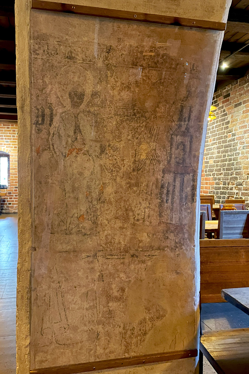 Tjock medeltida pelare i Norra längan. Rester av en målning av två gestalter med gloria är skyddade av plexiglas.
