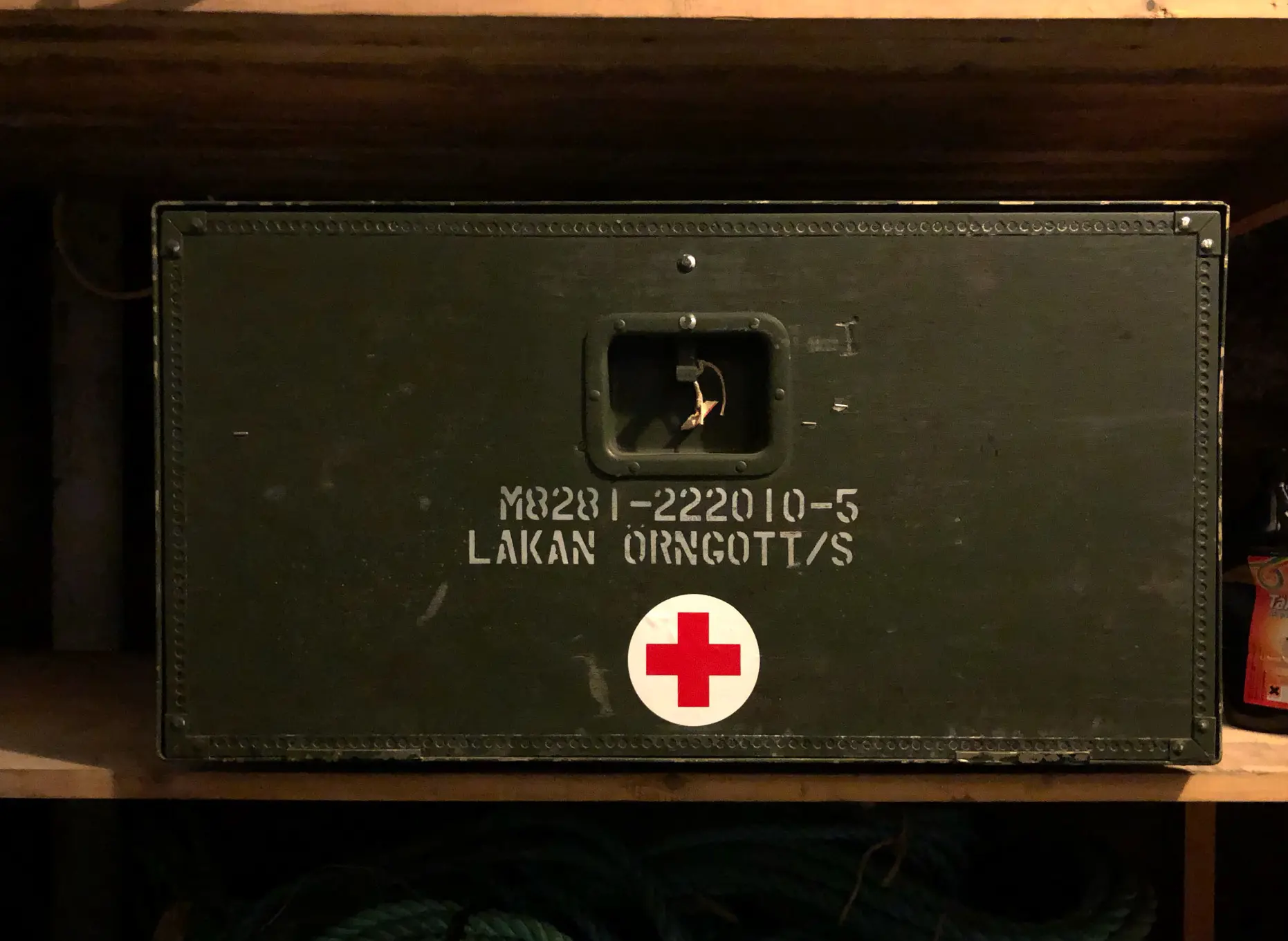 Närbild på mörkt grön box med ett rött kors. Märkt "lakan örngott".