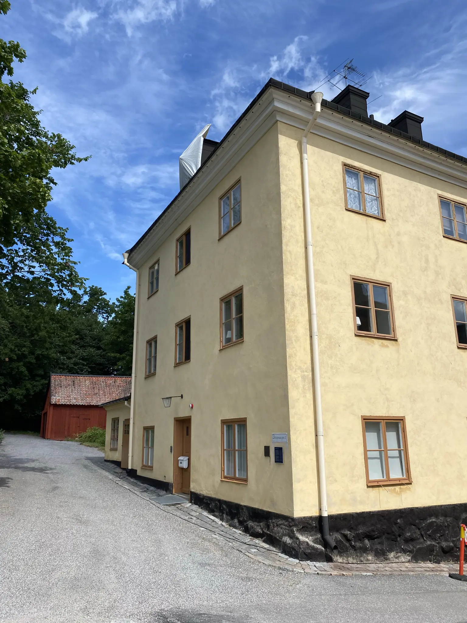 Stenvärdshuset på Malmen vid Drottningholm. Gul byggnad i tre våningar. I bakgrunden grönskande träd och ett rött uthus.
