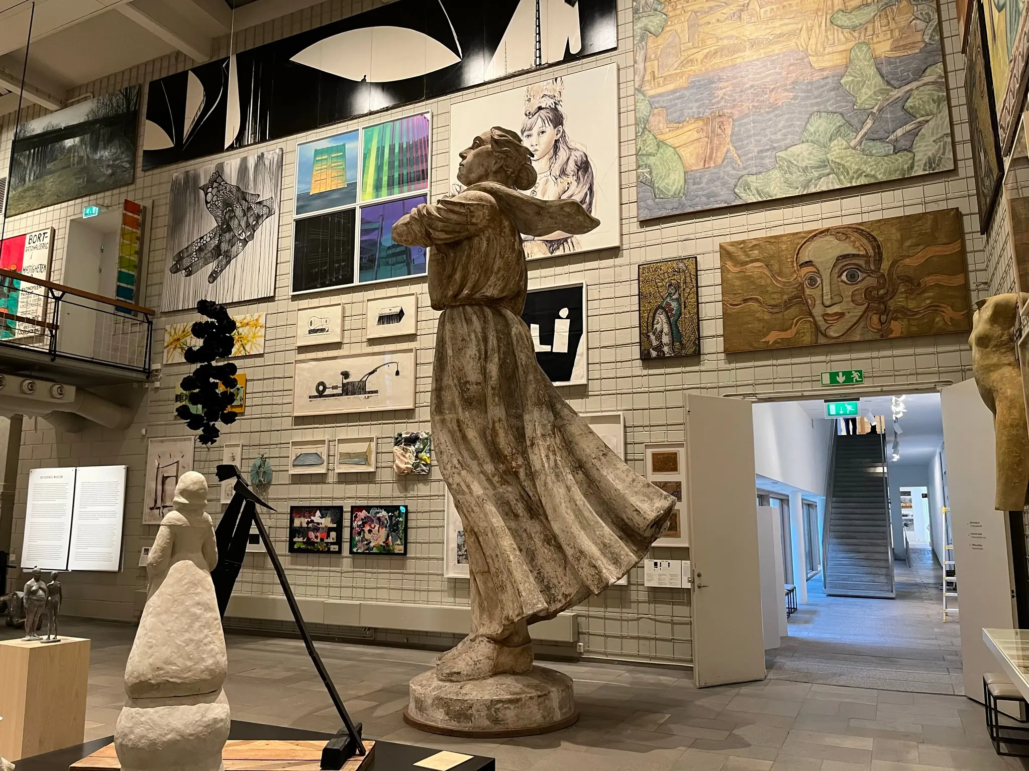 Skissernas museum. Utställningshall med konstverk från golv till tak. Mitt i rummet står en stor staty med svepande klänning.