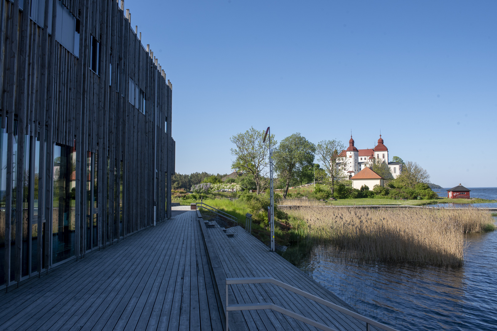 Naturum Vänerskärgårdens fasad mot vattnet och ett av de stora trädäcken. I bakgrunden syns Läckö slott.