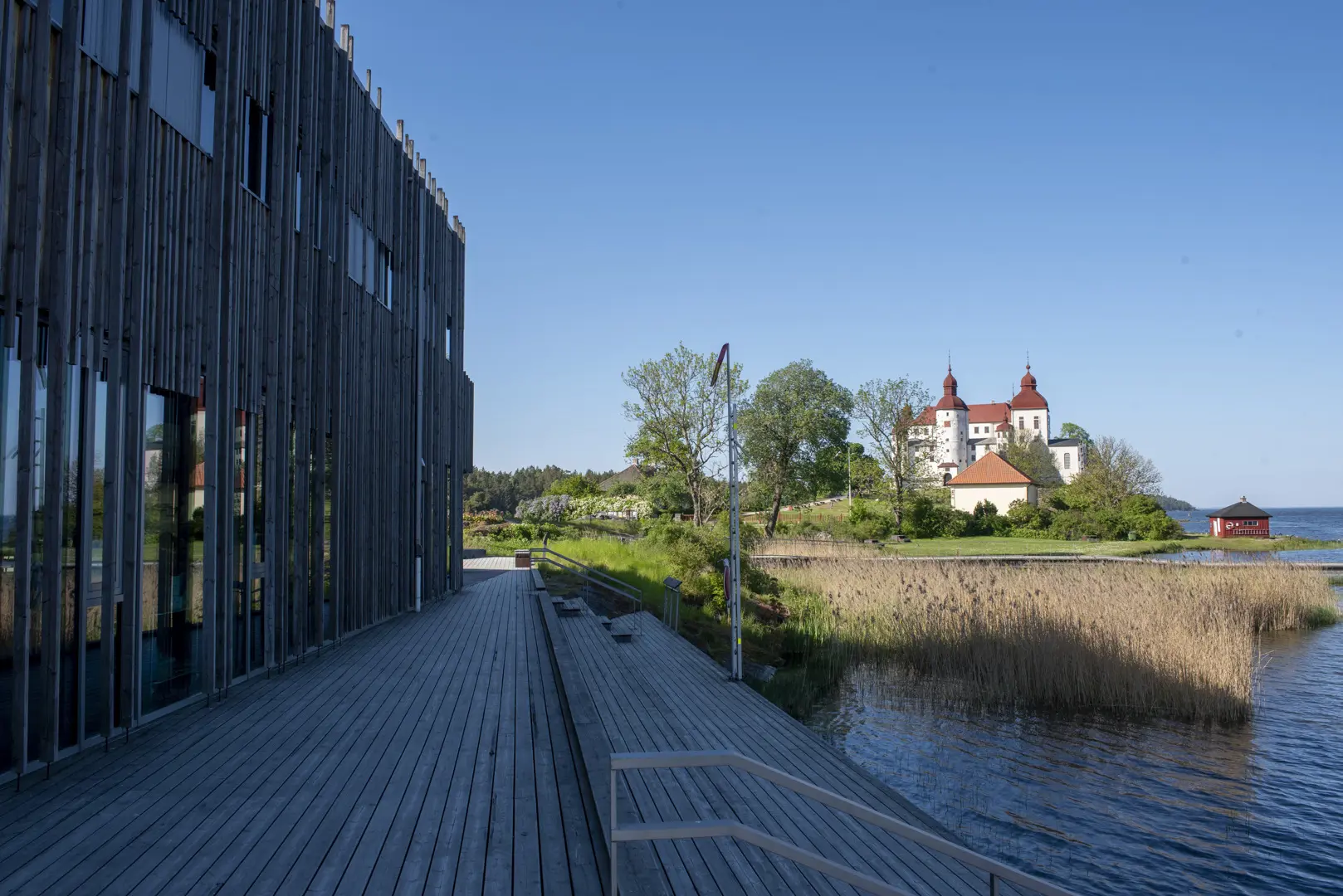 Naturum Vänerskärgårdens fasad mot vattnet och ett av de stora trädäcken. I bakgrunden syns Läckö slott.