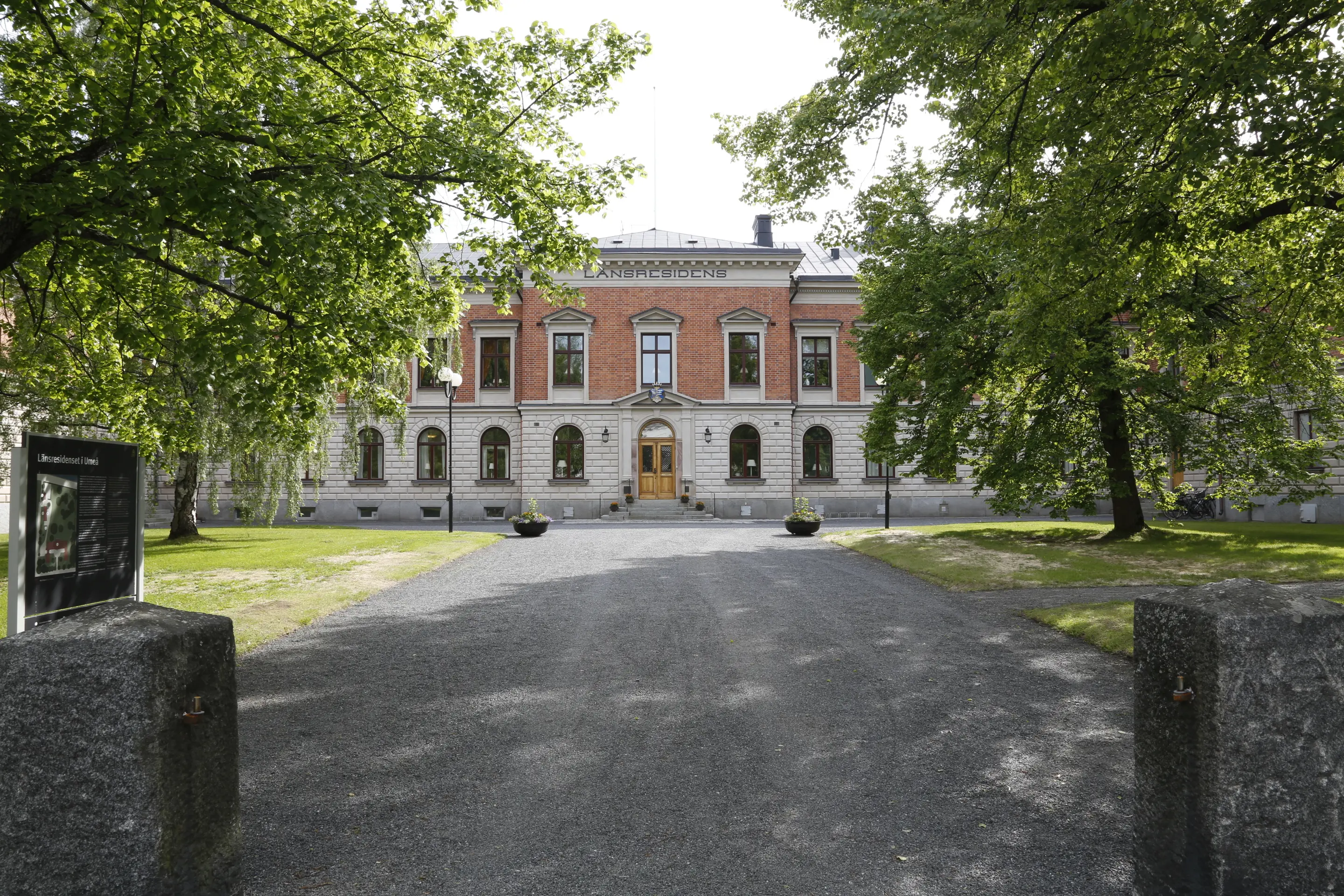 Entréfasaden, Umeå residens. En tvåvåningsbyggnad i tegel och vit puts. Sommar och grönska.