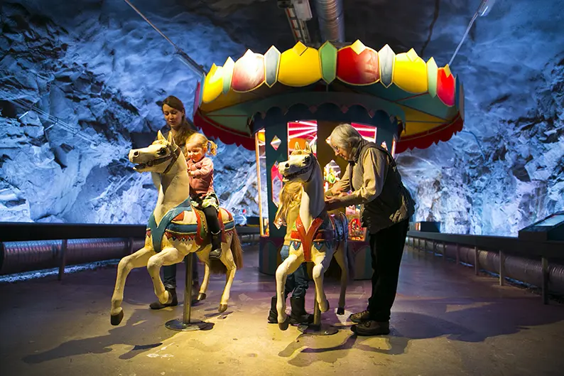 Karuell på museumet. Syskonpar med mamma och mormor undersöker karusellhästarna.