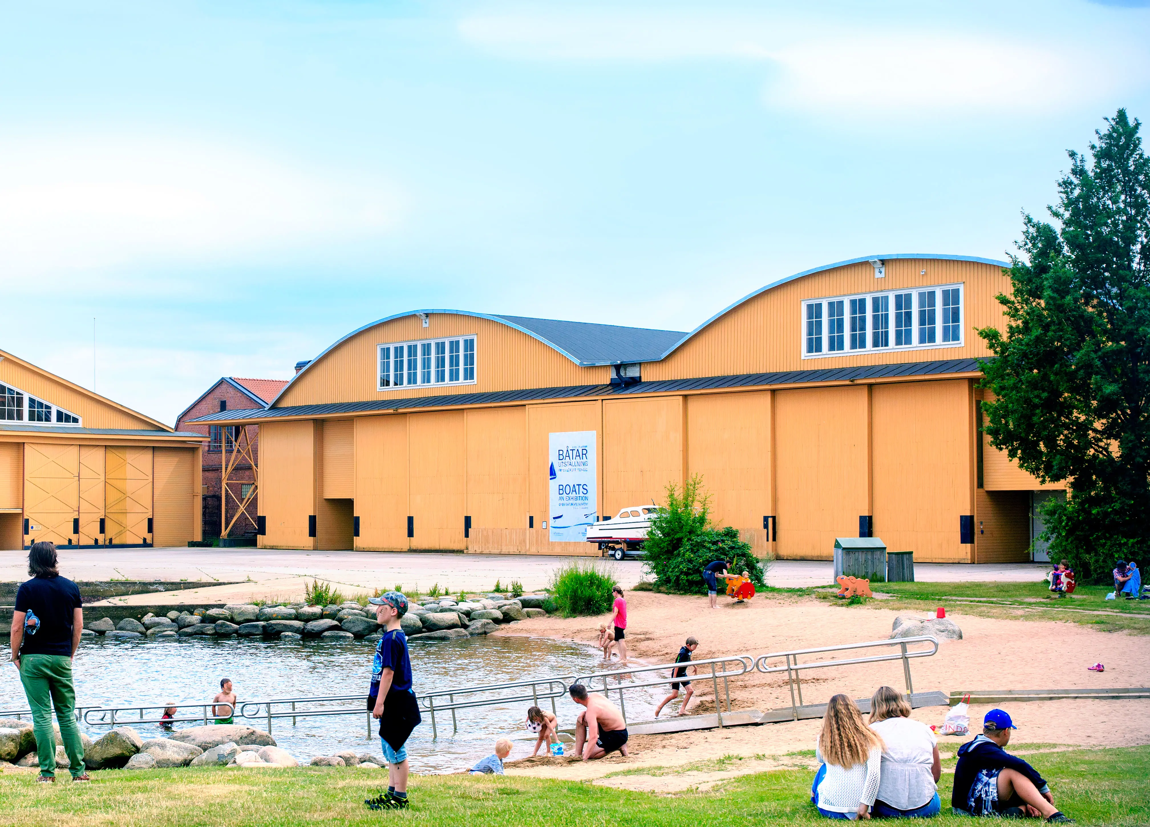 Gula byggnader med välvda tak. I förgrunden människor som badar i en vik.